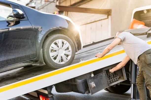 Person loading a black car onto a flatbed tow truck.