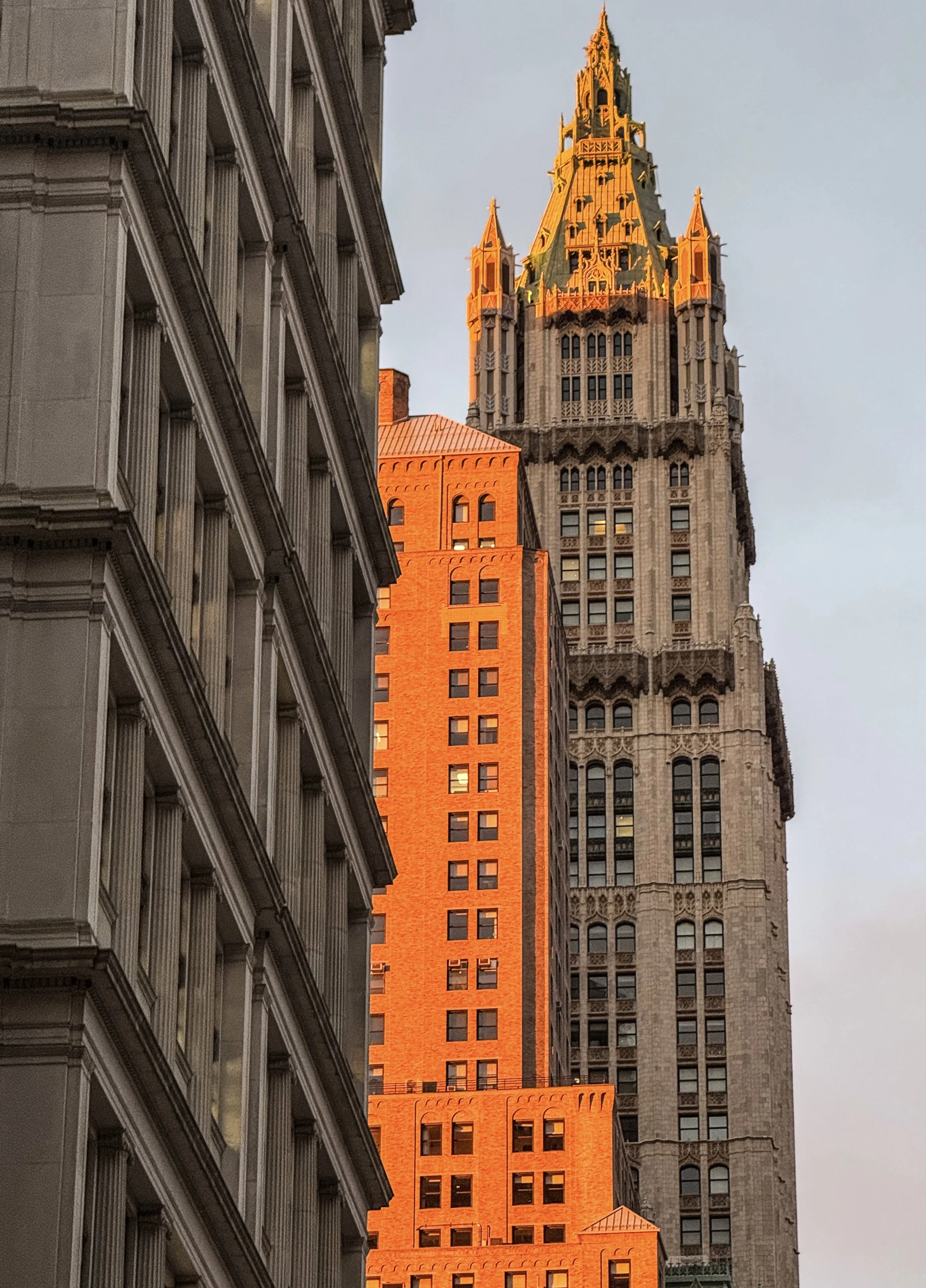 Sunset light illuminating the tops of skyscrapers in a city, including one with a spire.