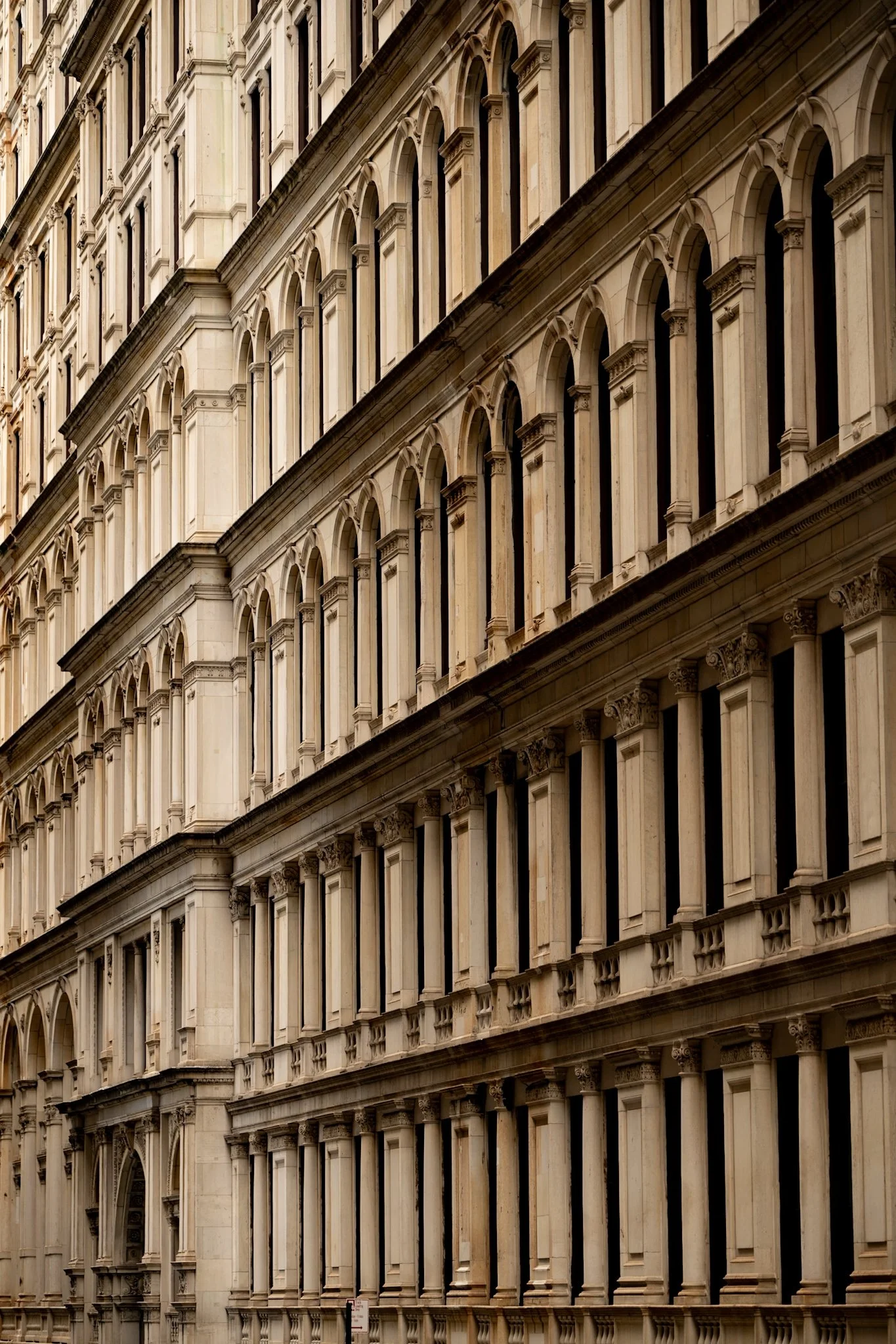 Close-up of a beige stone building with multiple arched windows and decorative architectural details, viewed from a slight angle.