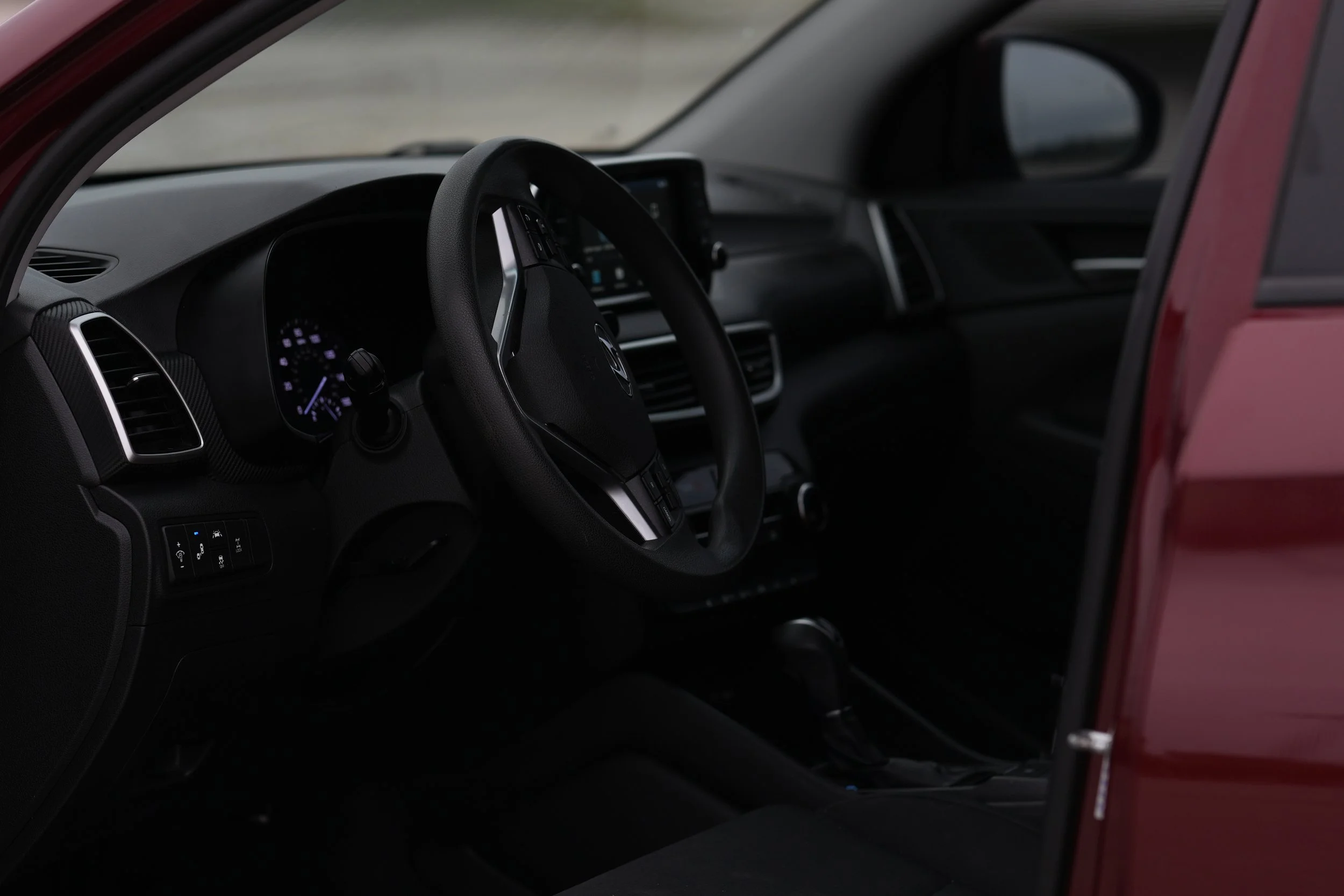 Interior view of a car showing the steering wheel, dashboard, and part of the windshield. The vehicle has a black interior with digital controls and a touchscreen display.