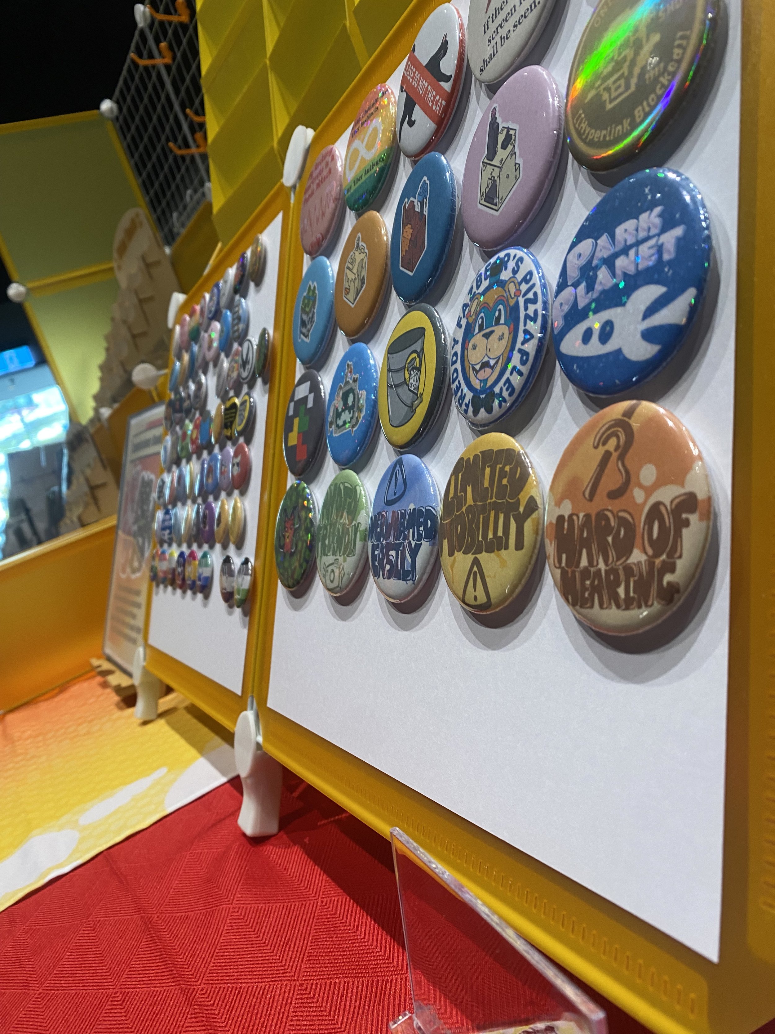 Colorful round buttons with various stickers and messages displayed on a white board, with a yellow frame and a red tablecloth.