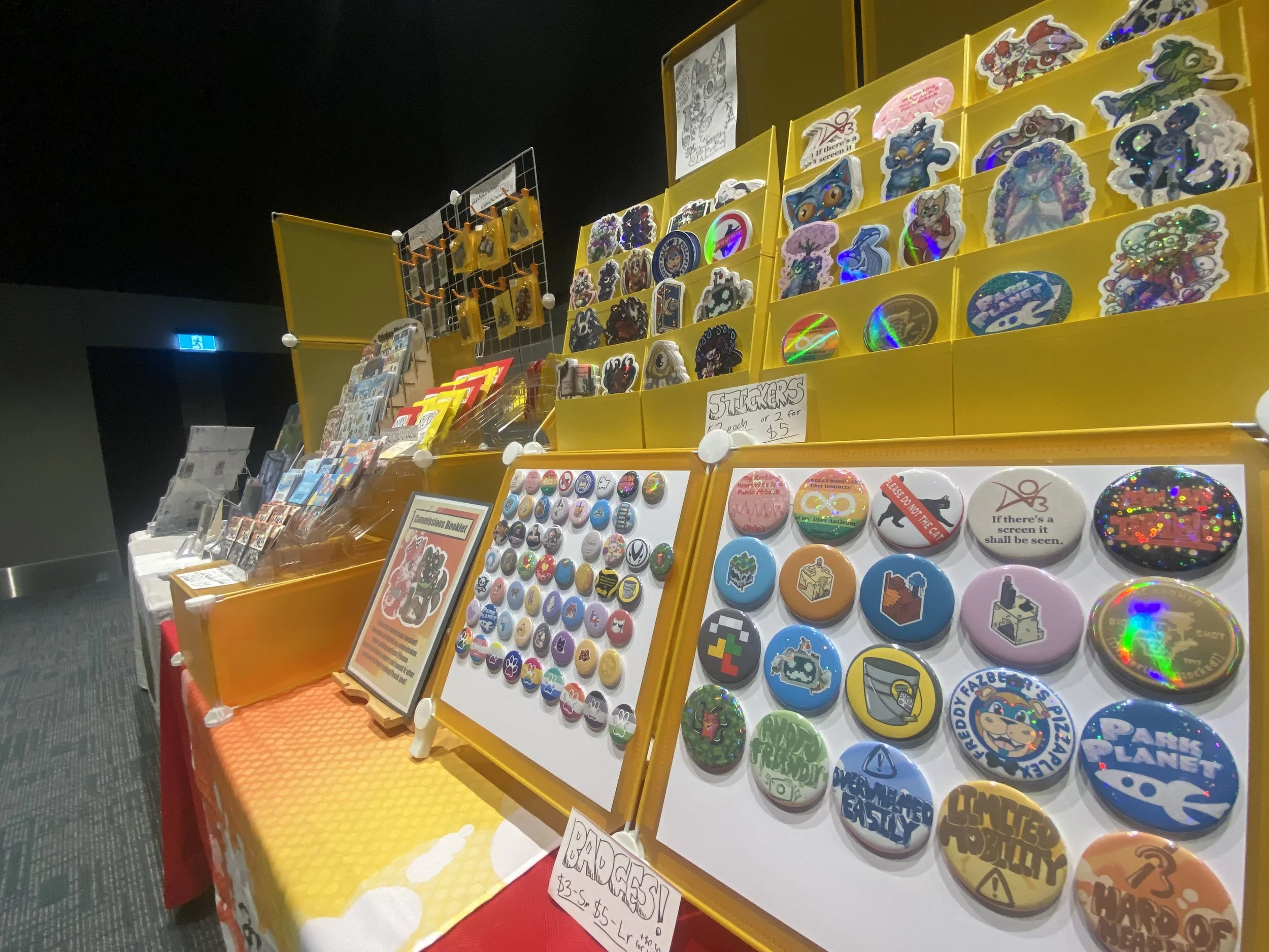 Display of colorful stickers and buttons on yellow and white boards at a sale table, with some prices and signs visible.