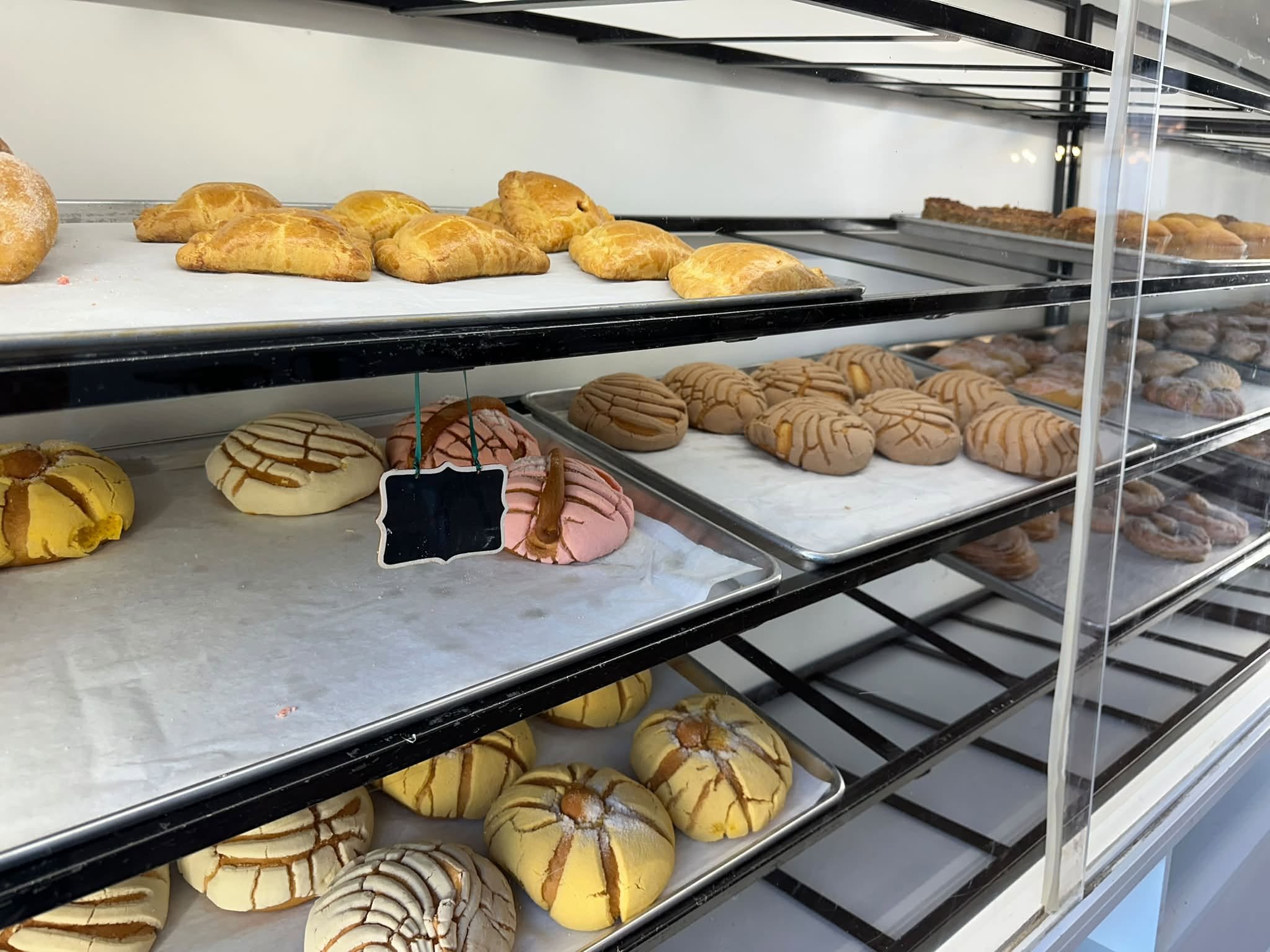 Display case with assorted baked pastries, including croissants, cookies, and buns on multiple shelves.