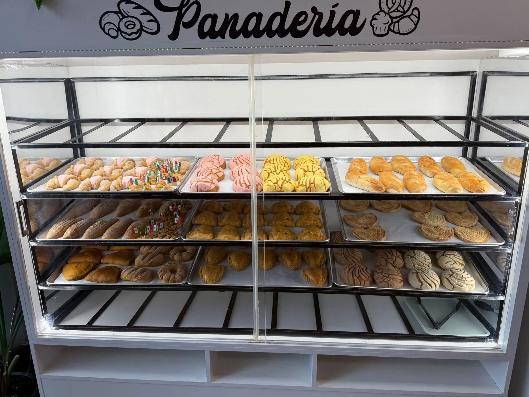 Display case filled with various cookies including pink frosted, yellow, croissants, and other pastries.