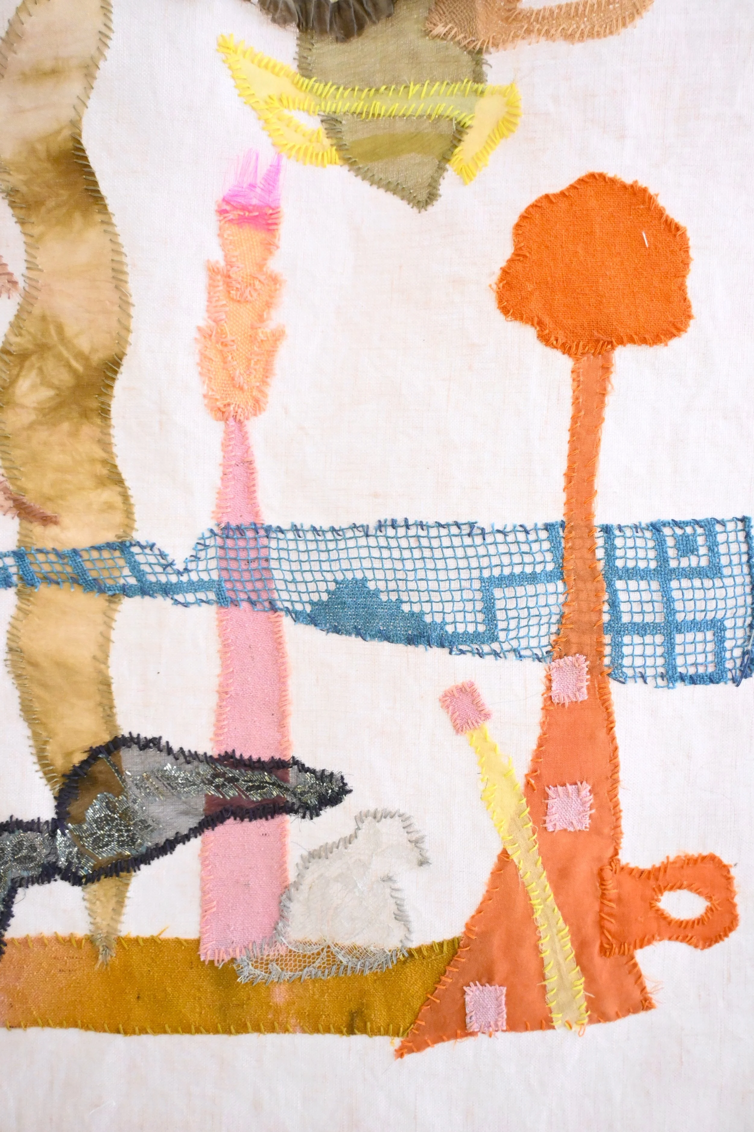 Close-up of a fabric embroidery with various colors and textures, including images of plant-like shapes and a fish, stitched onto a white background.