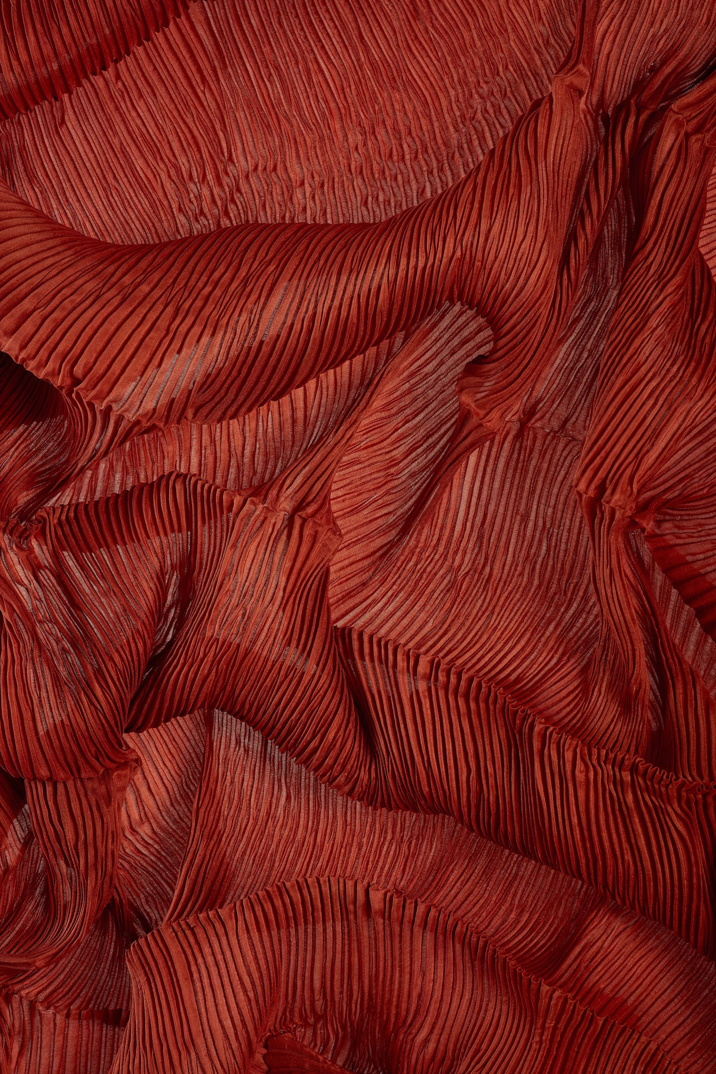 Close-up of red pleated fabric with flowing, wavy texture and lines.