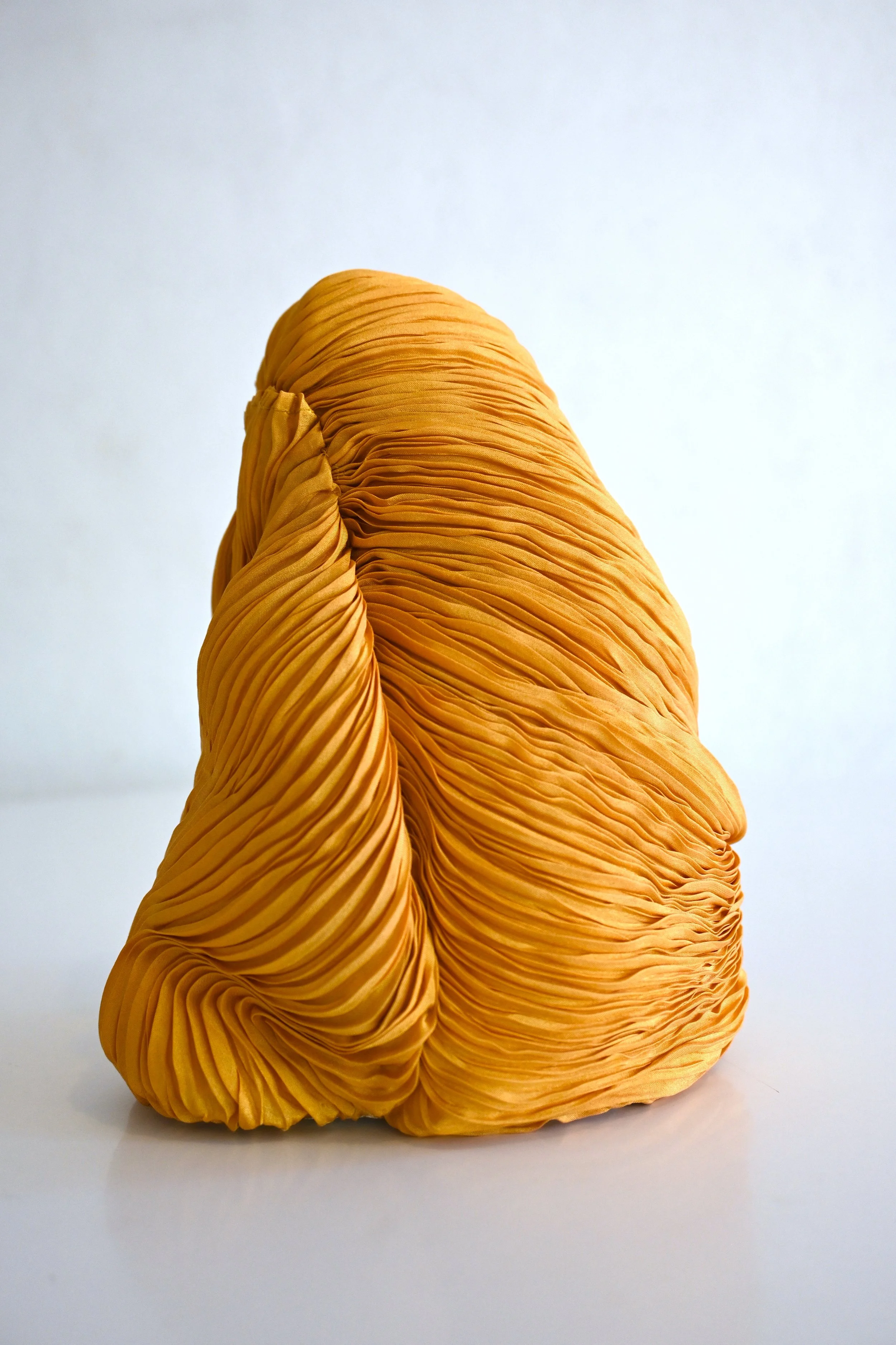 Close-up of an orange pleated fabric sculpture against a white background.