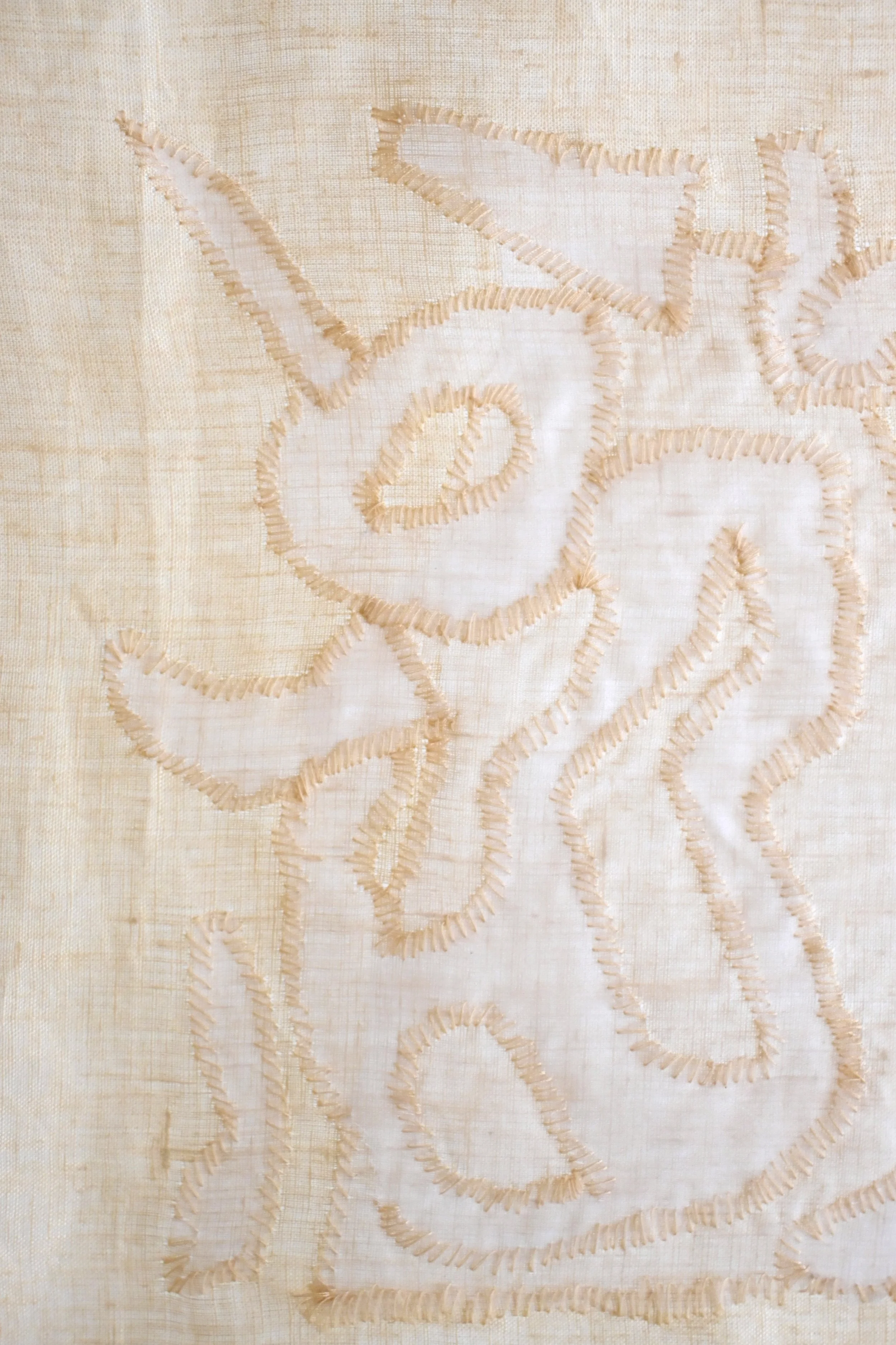 Close-up of embroidered floral design on fabric with beige and cream colors, featuring stitched outlines.