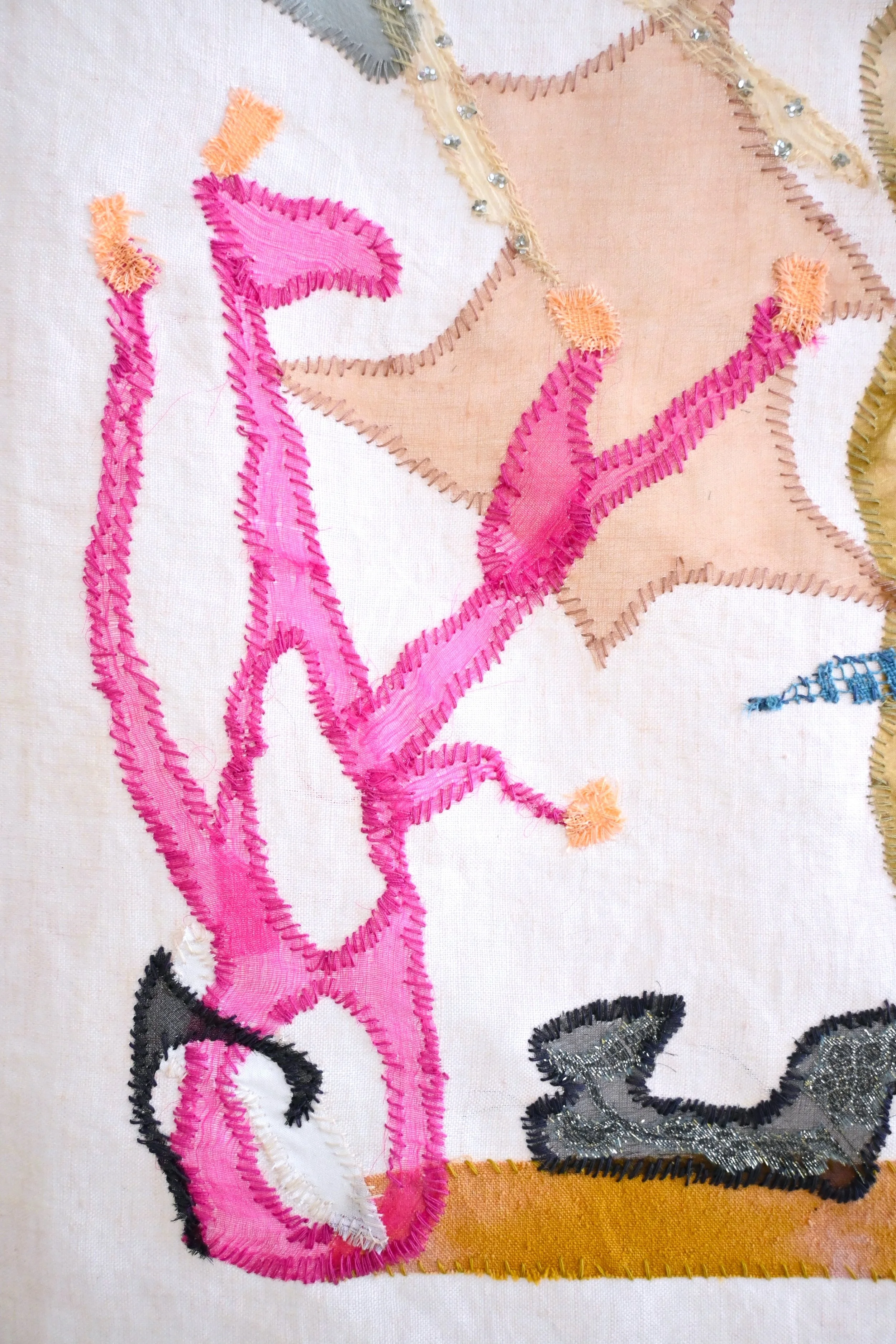 Close-up of embroidered floral design on fabric with pink, beige, gray, black, and silver threads.