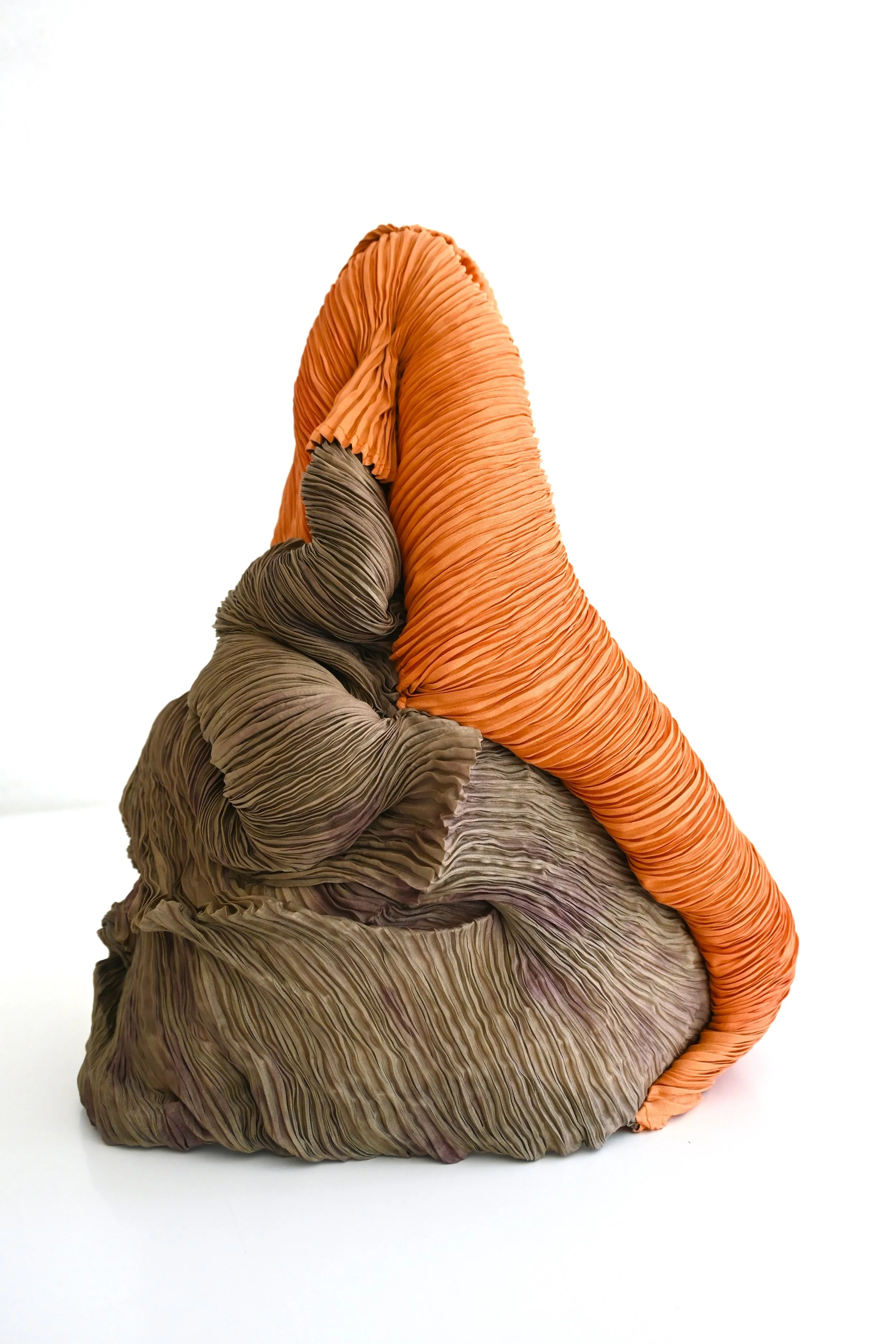 A sculpture resembling a mountain of crumpled, textured fabric with orange, brown, and gray tones.