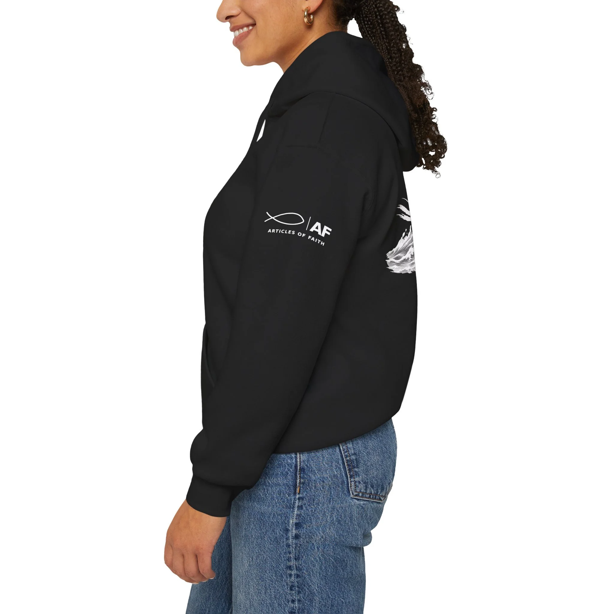 Side view of a smiling woman wearing a black hoodie with a logo and text on the sleeve, and blue jeans.