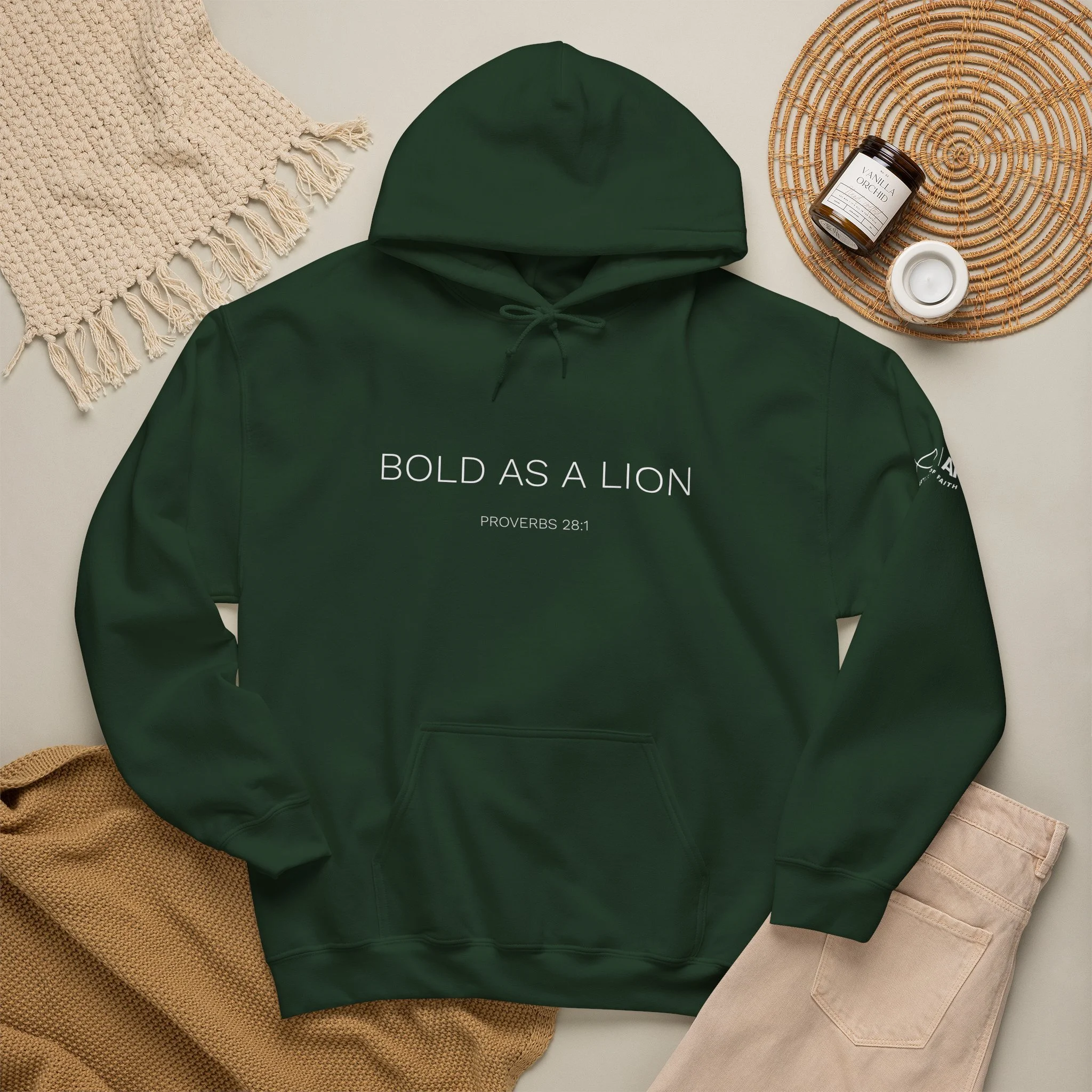 A green hoodie with the text 'Bold as a Lion' and a Bible verse, Lifestyle flat lay featuring Articles of Faith Scripture-inspired apparel  with BOLD AS A LION on the front.
