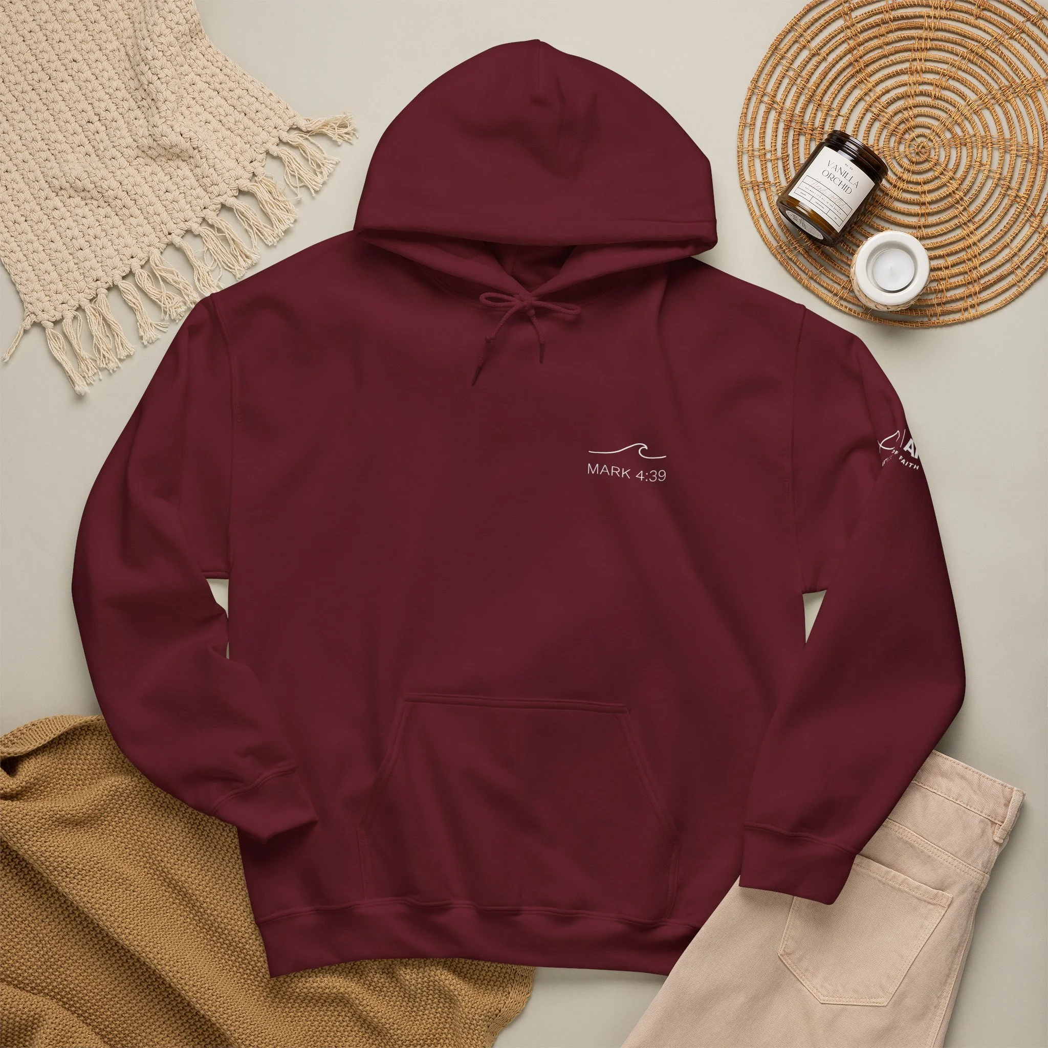 A burgundy hoodie with a quote, Lifestyle flat lay featuring Articles of Faith Scripture-inspired apparel with MARK 4:39 on the front
