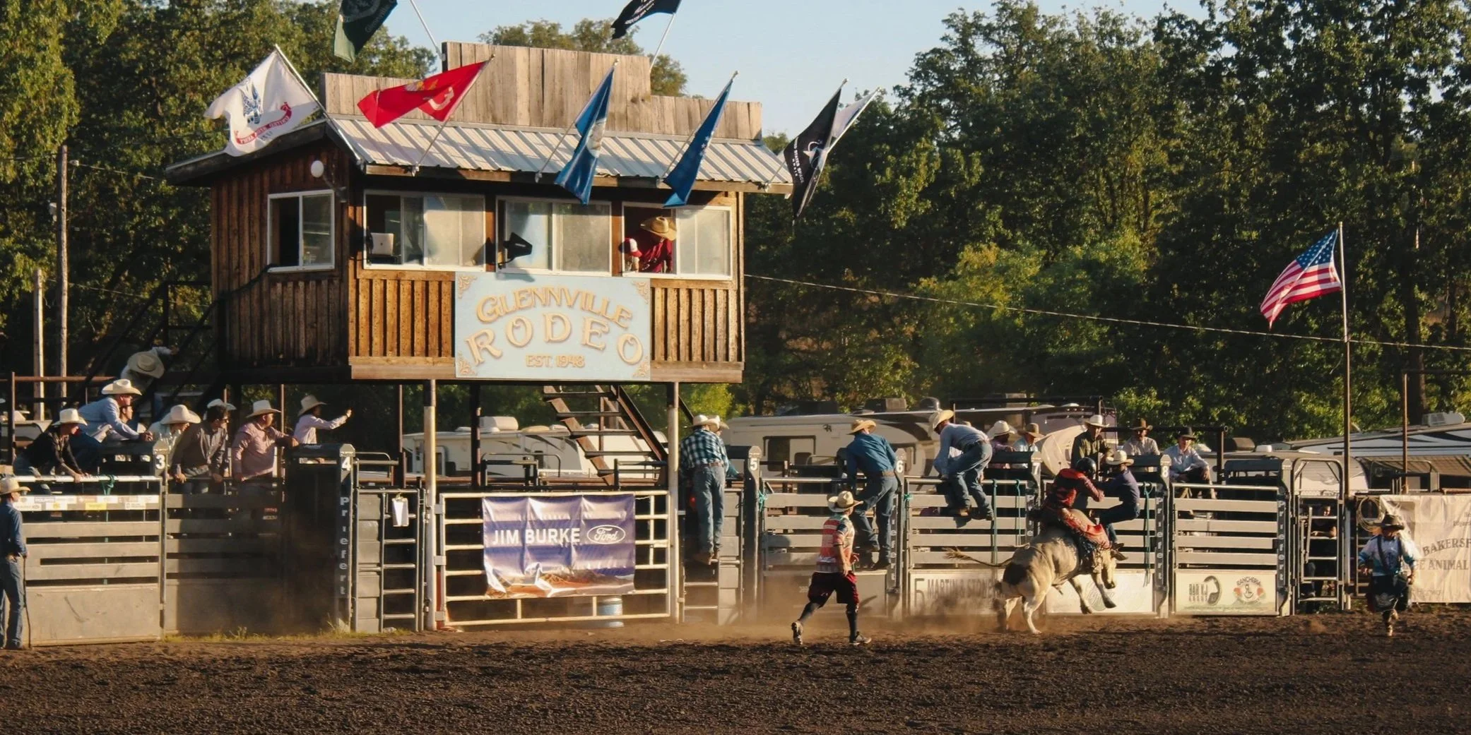 Glennville Rodeo arena with cowboys, spectators, flags, and a rider on horseback in the dirt ring