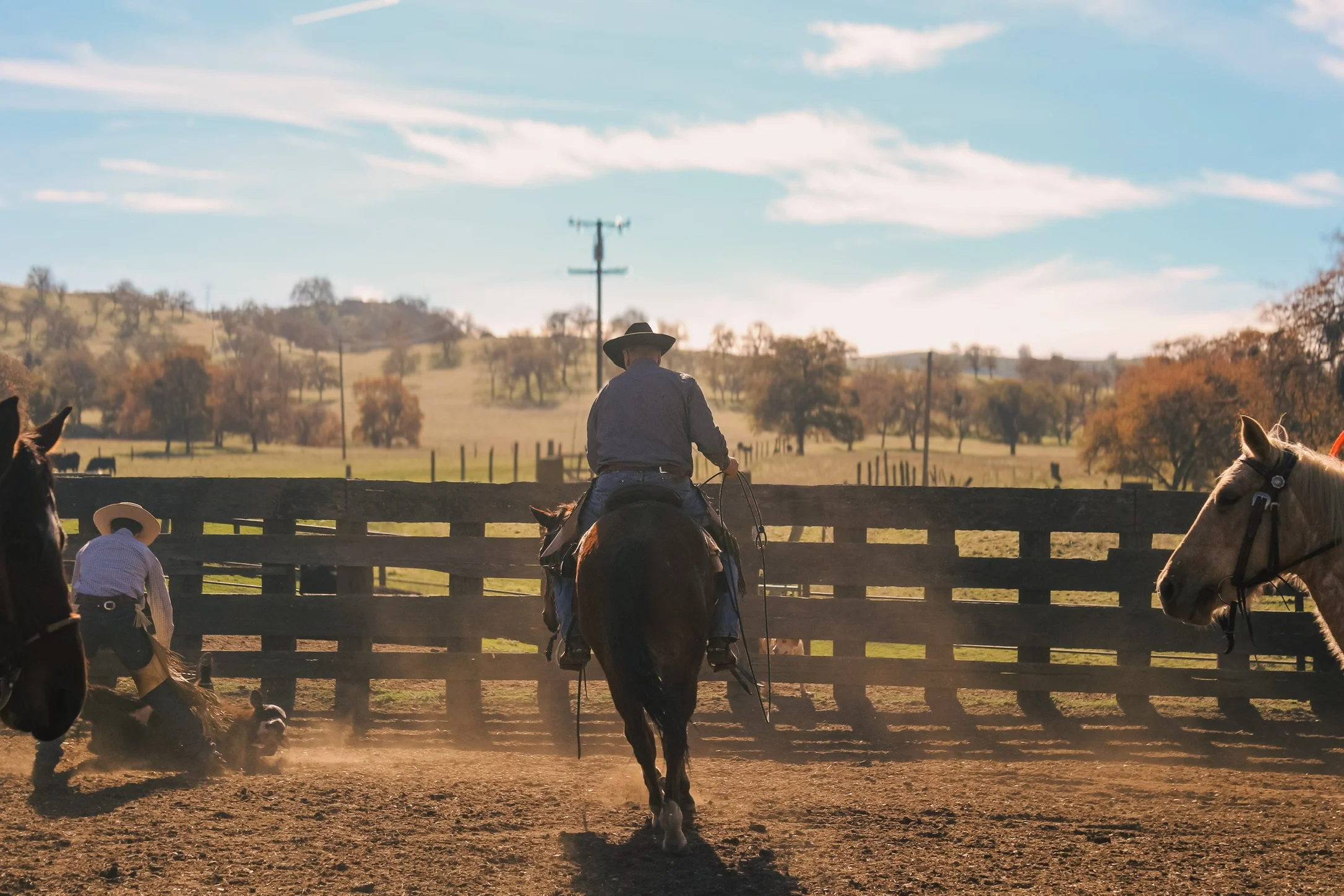 Cowboys on horseback in a fenced ranch arena overlooking California rolling hills