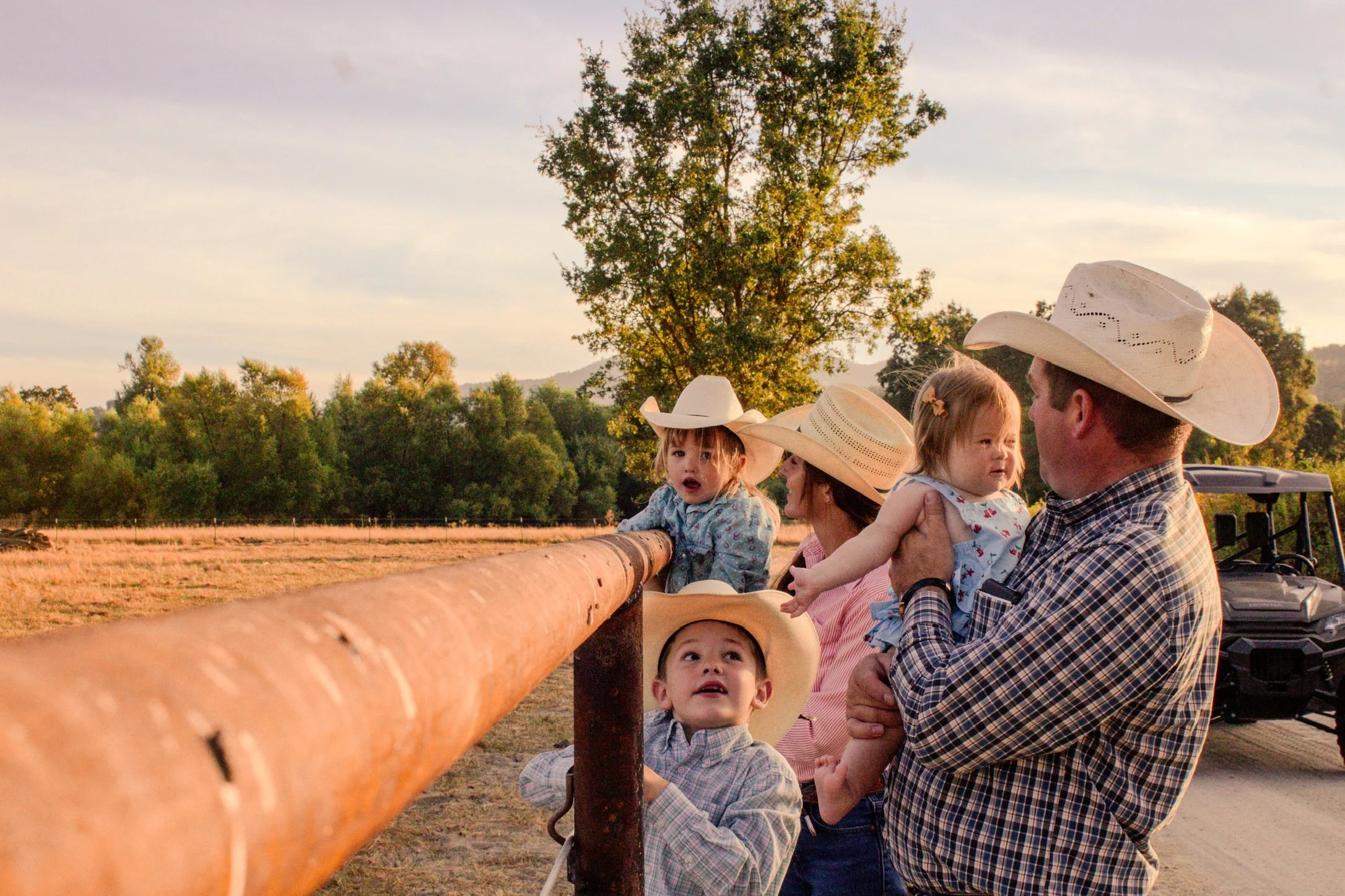 Family wearing cowboy hats riding on a hay wagon through a sunlit field