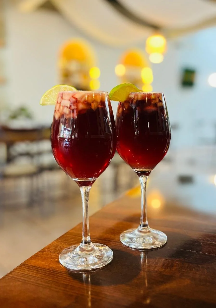 Dos copas de vino tinto con rodajas de limón y lima en la orilla, en un restaurante con decoración tropical y luces cálidas.