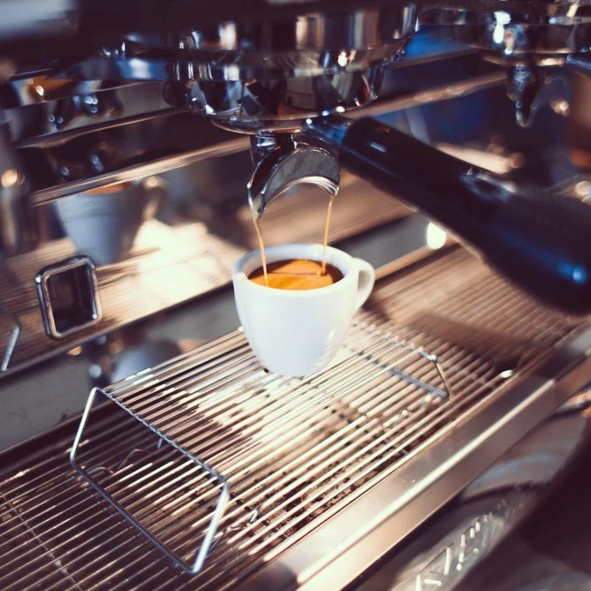 Un espresso siendo preparado en una máquina de café espresso profesional, con una taza blanca bajo el mecanismo de salida del café.