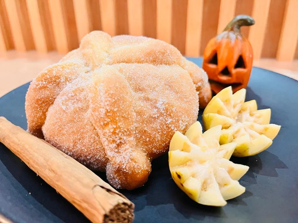 Calaveras de azúcar, una calabaza de Halloween tallada en madera, cortadores de fruta, y una rama de canela en un plato negro.