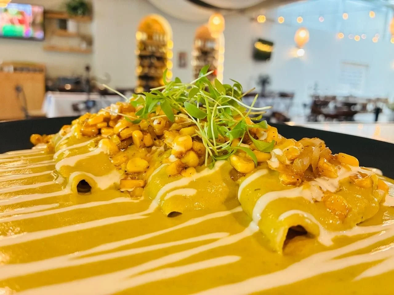 Plato con pasta envuelta con salsa amarilla, cubierto con pico de gallo y un adorno de microgreens.