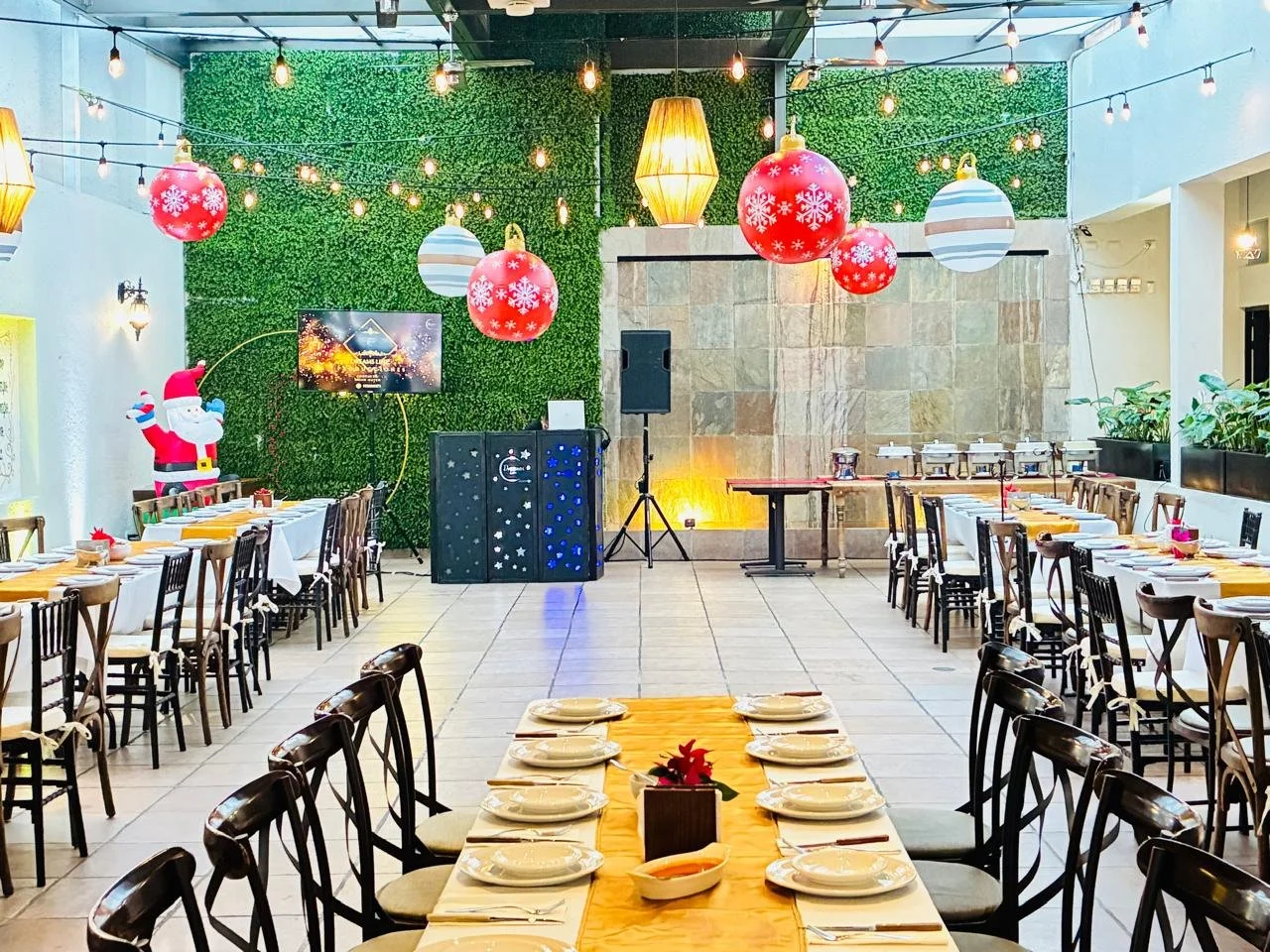 Sala decorada para una celebración navideña con mesas arregladas y adornos como bolas navideñas, luces y un varón de nieve inflable, preparado para una fiesta.