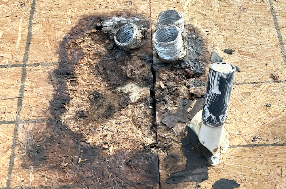 Close-up of a damaged wooden surface with metal pipes protruding and blackened areas, indicating fire or heat damage.