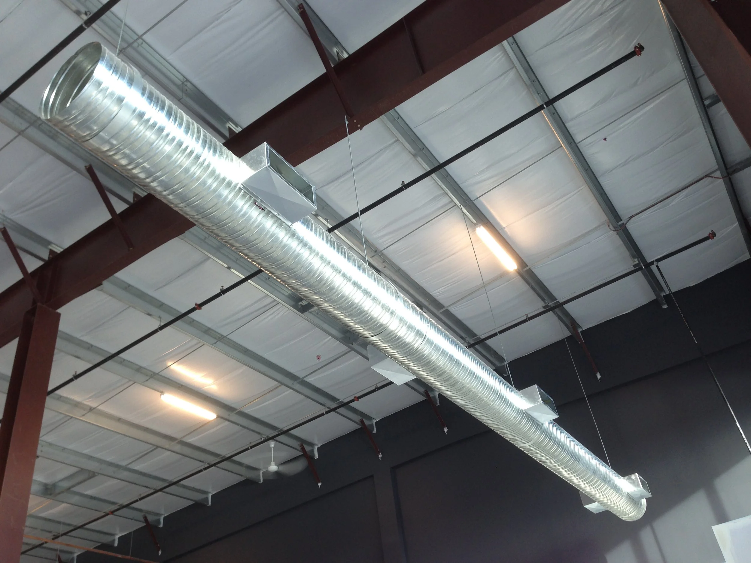 Interior of a large industrial warehouse with a high ceiling, metal ventilation duct, and exposed metal beams.