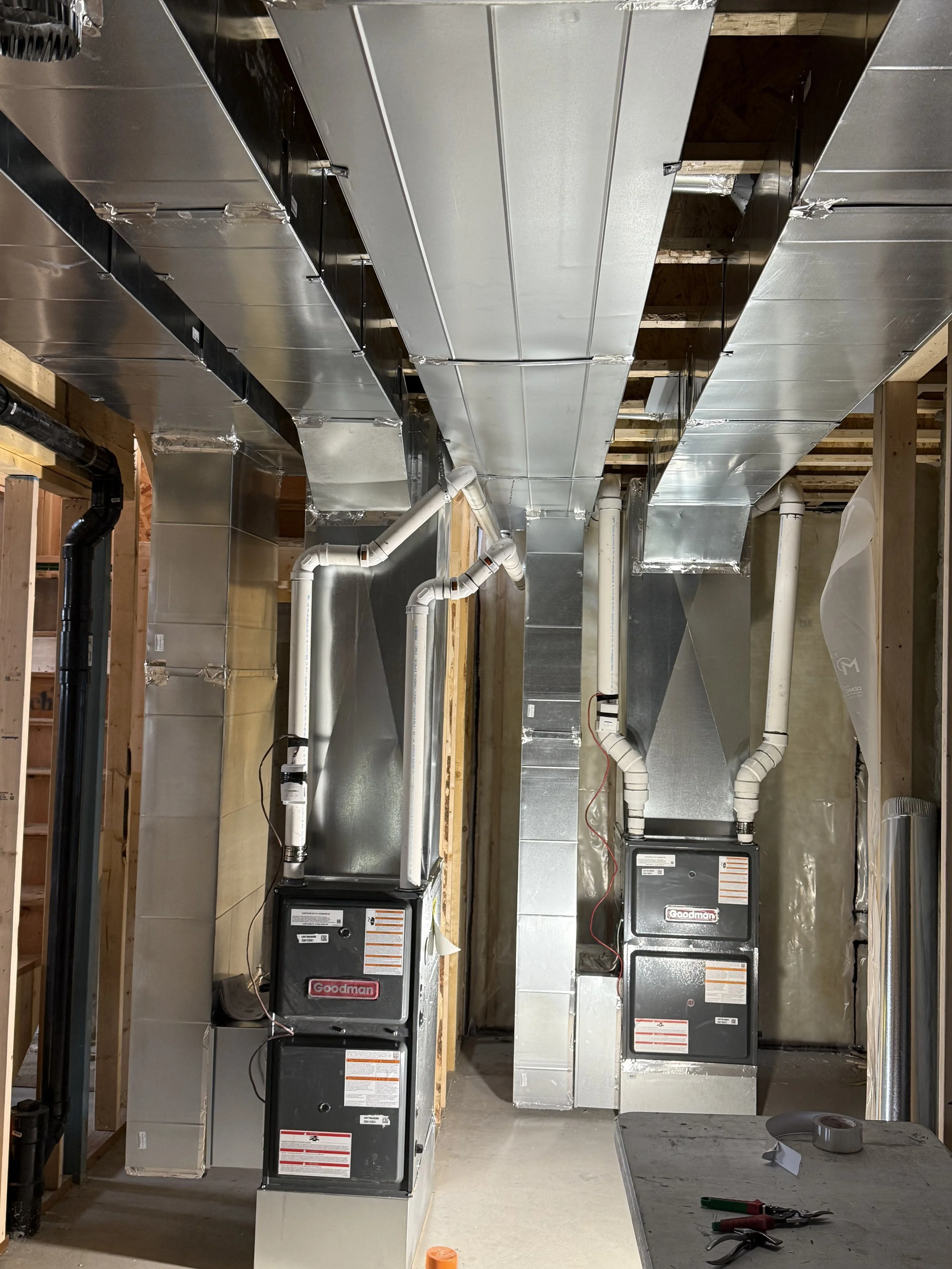 A room with HVAC units and ductwork installed on the ceiling. Tools and tape on a work table are visible in the foreground.