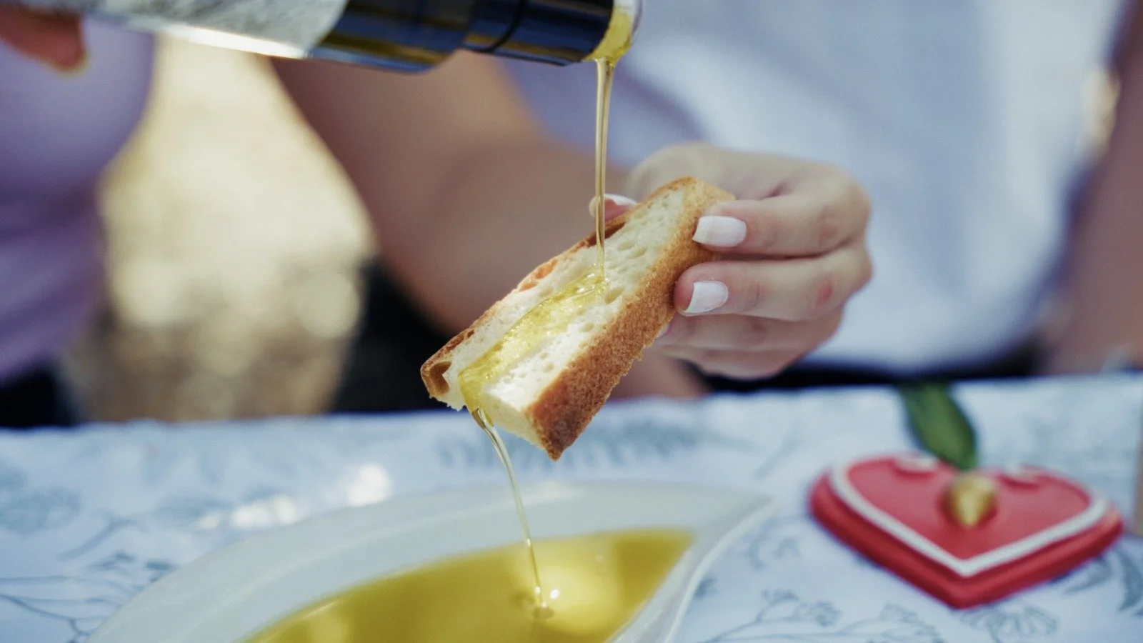 Person pouring honey onto a slice of bread with butter, on a white plate.