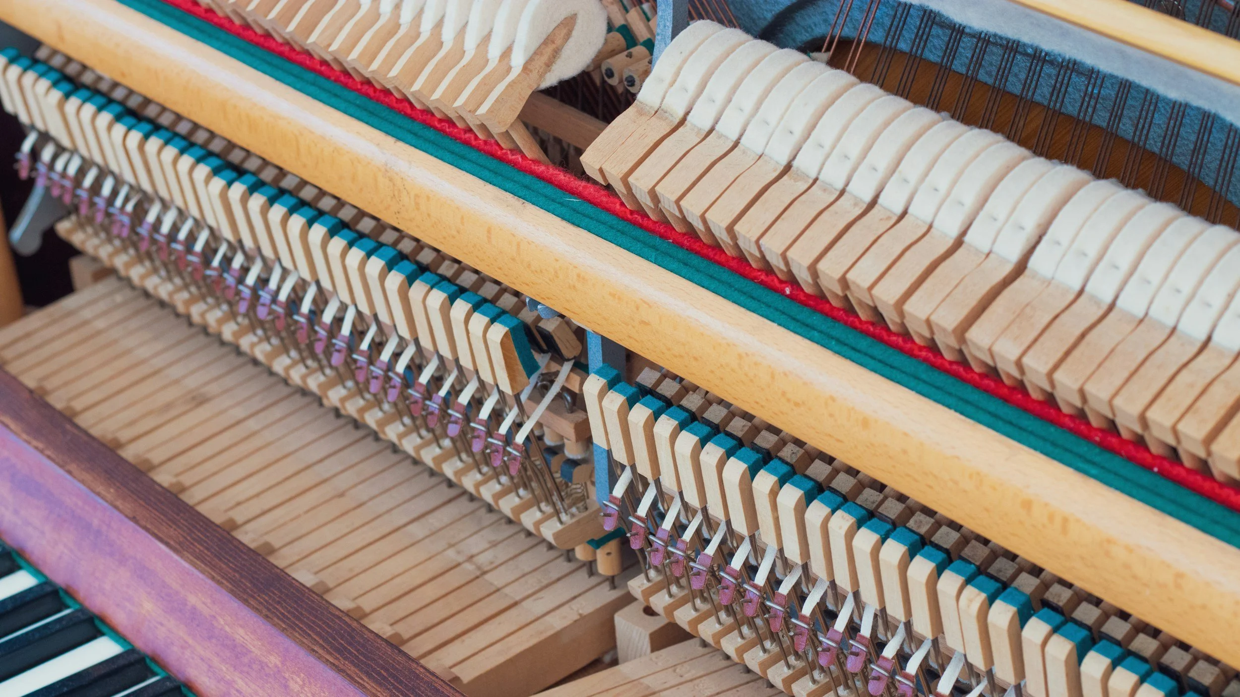 The inside of a piano with visible wooden and metal components, including strings, hammers, and keys.
