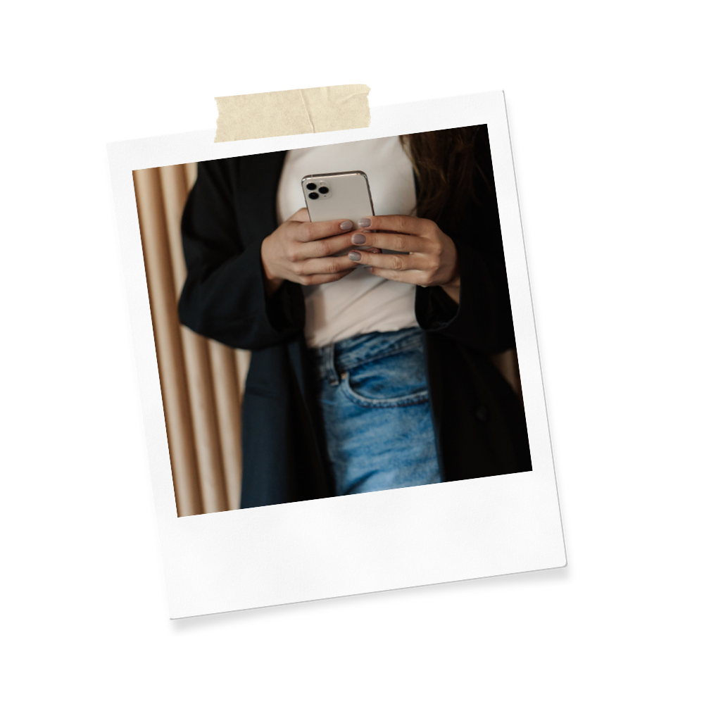 Person holding a smartphone while standing indoors with curtains in the background.