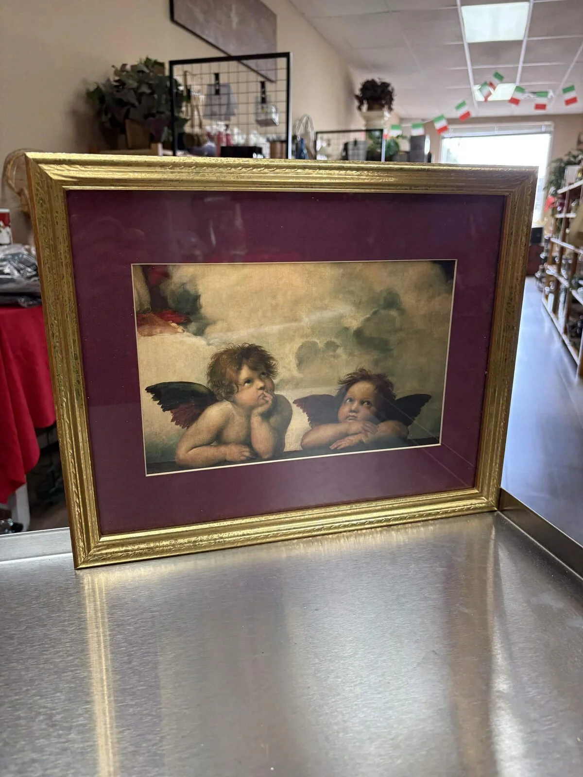 Two cherubs pictured in burgundy matting and a gold-tone frame, photographed inside the shop
