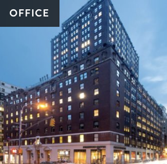 An urban building with a modern glass upper section and a traditional brick lower section, illuminated at dusk.