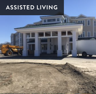 Front entrance of a building labeled 'Assisted Living' with vehicles parked in front, under a clear sky.