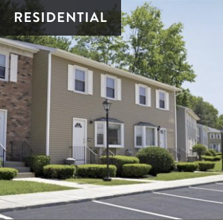 Exterior of a residential apartment complex with neatly maintained bushes, a lamp post, and parking spaces in front.