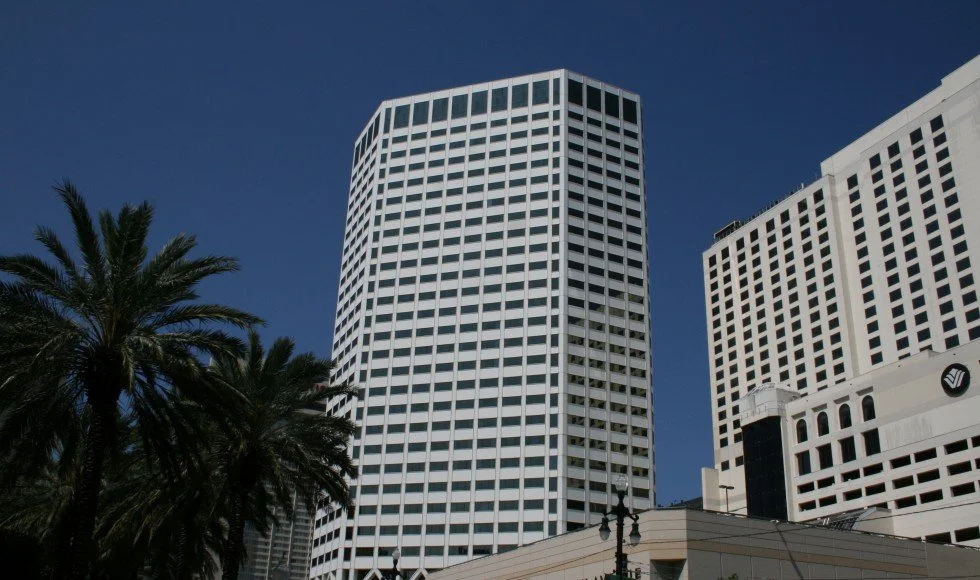 Tall modern office buildings with white exteriors against a clear blue sky, palm trees in the foreground.