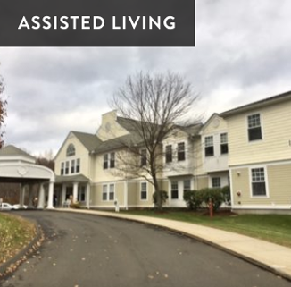 Assisted living residential building with a curved driveway, leafless tree, and a partly cloudy sky
