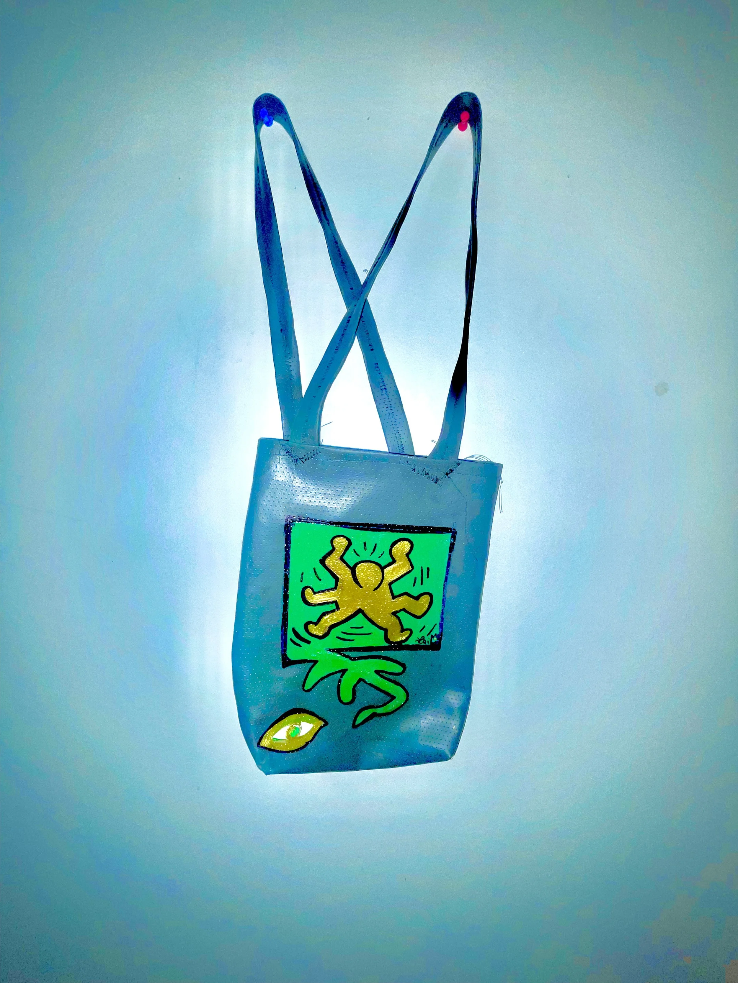 A face mask with a colorful abstract design, featuring a yellow figure with multiple limbs, a single eye, and an eye symbol at the bottom.