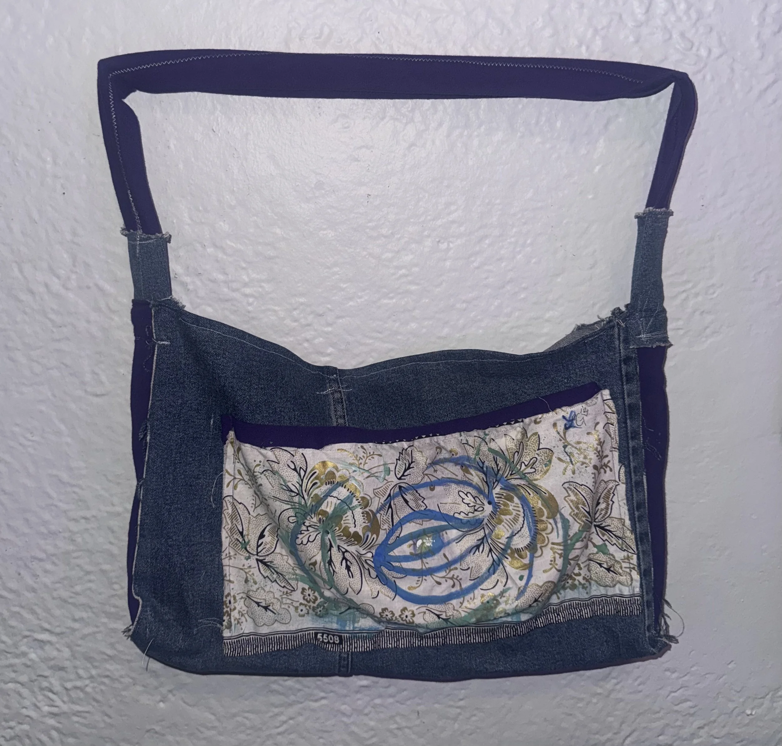 A pair of denim shorts with embroidered floral and dragon design on the front, hanging against a white textured wall.