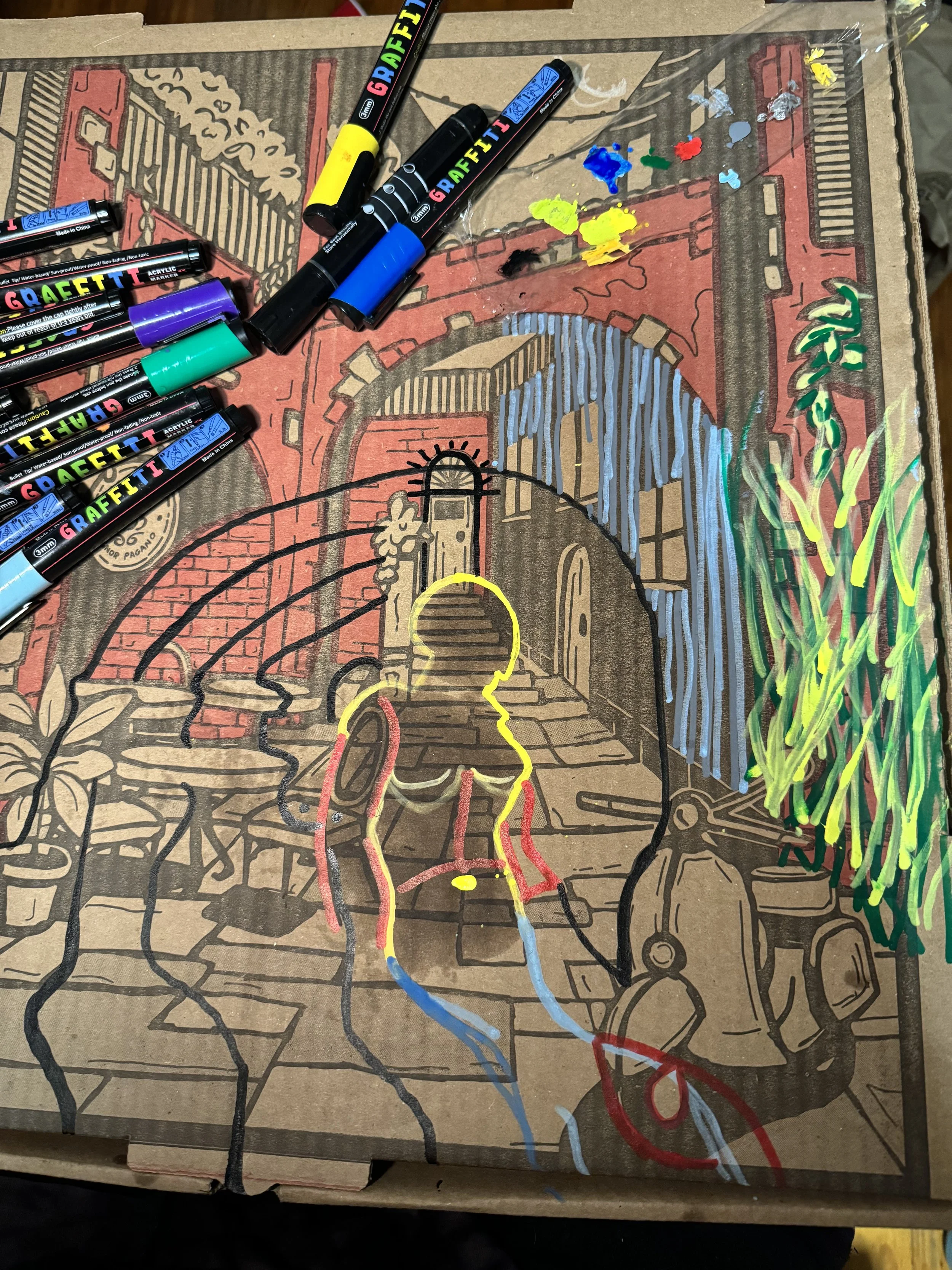 A coloring page featuring a cityscape with a bridge, building, and stairs. Colorful markers are placed on top, with paint splatters on the page. The drawing includes a silhouette of a person outlined in yellow, red, and blue.