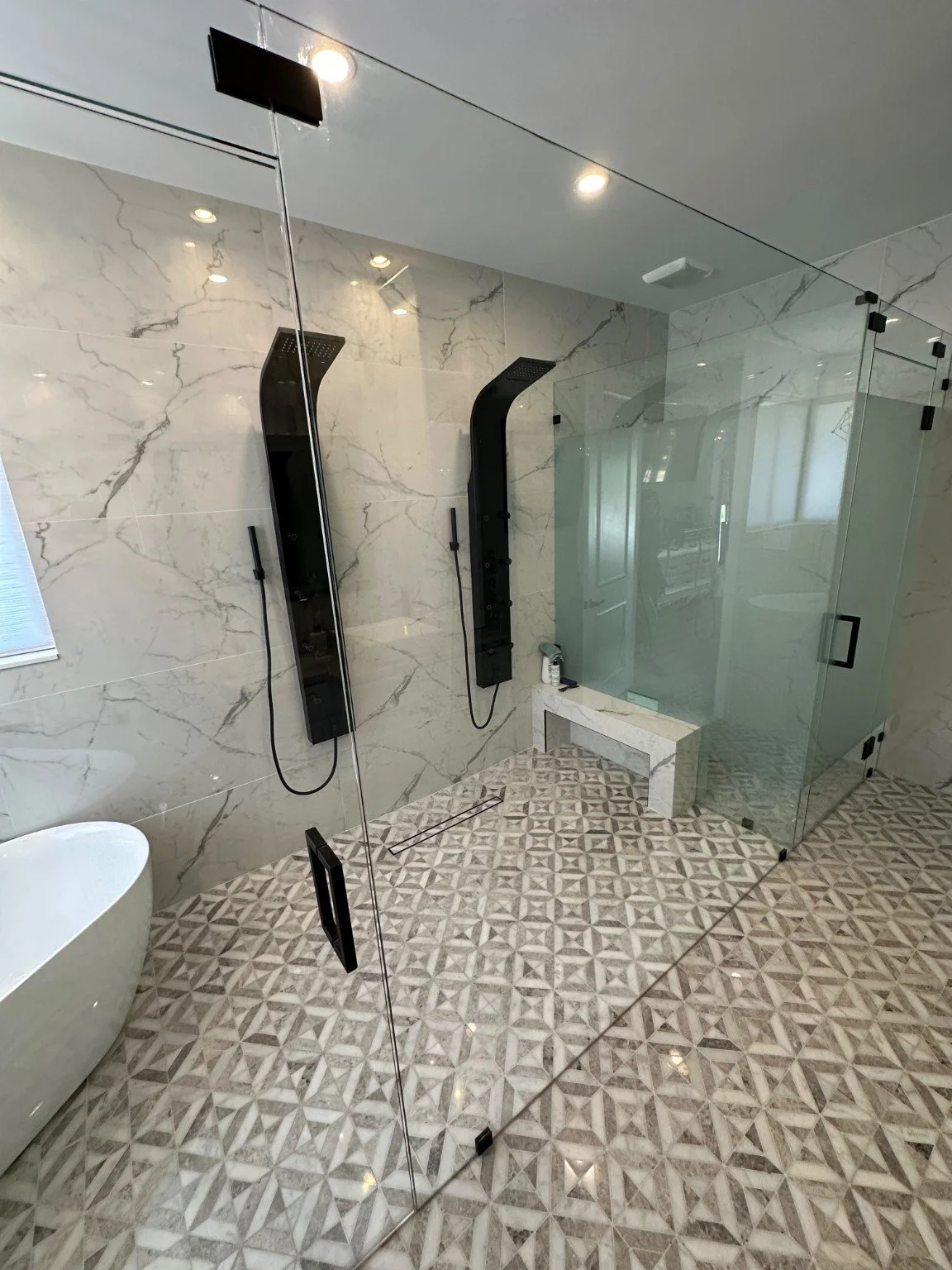 Frameless glass shower with marble-look tile and black fixtures.
