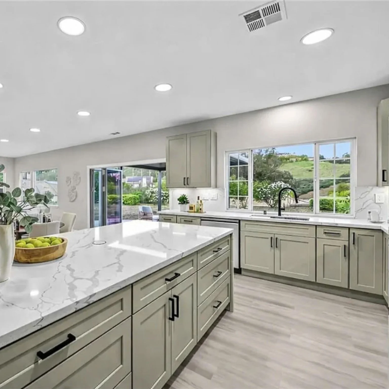 Sage-toned kitchen cabinets with white marble-look countertops and black fixtures.