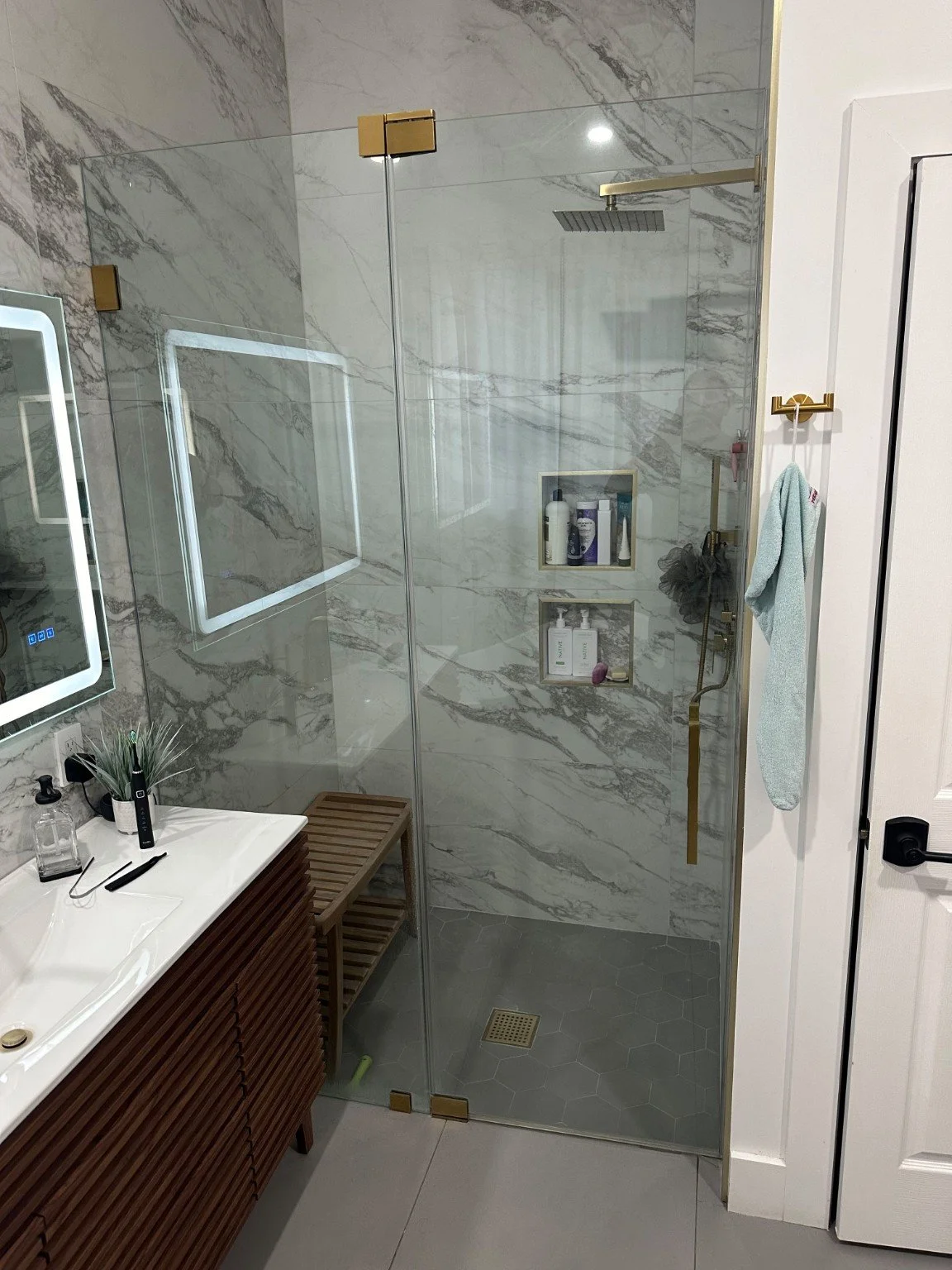 Glass shower with marble-look walls, recessed niches, and gold fixtures.