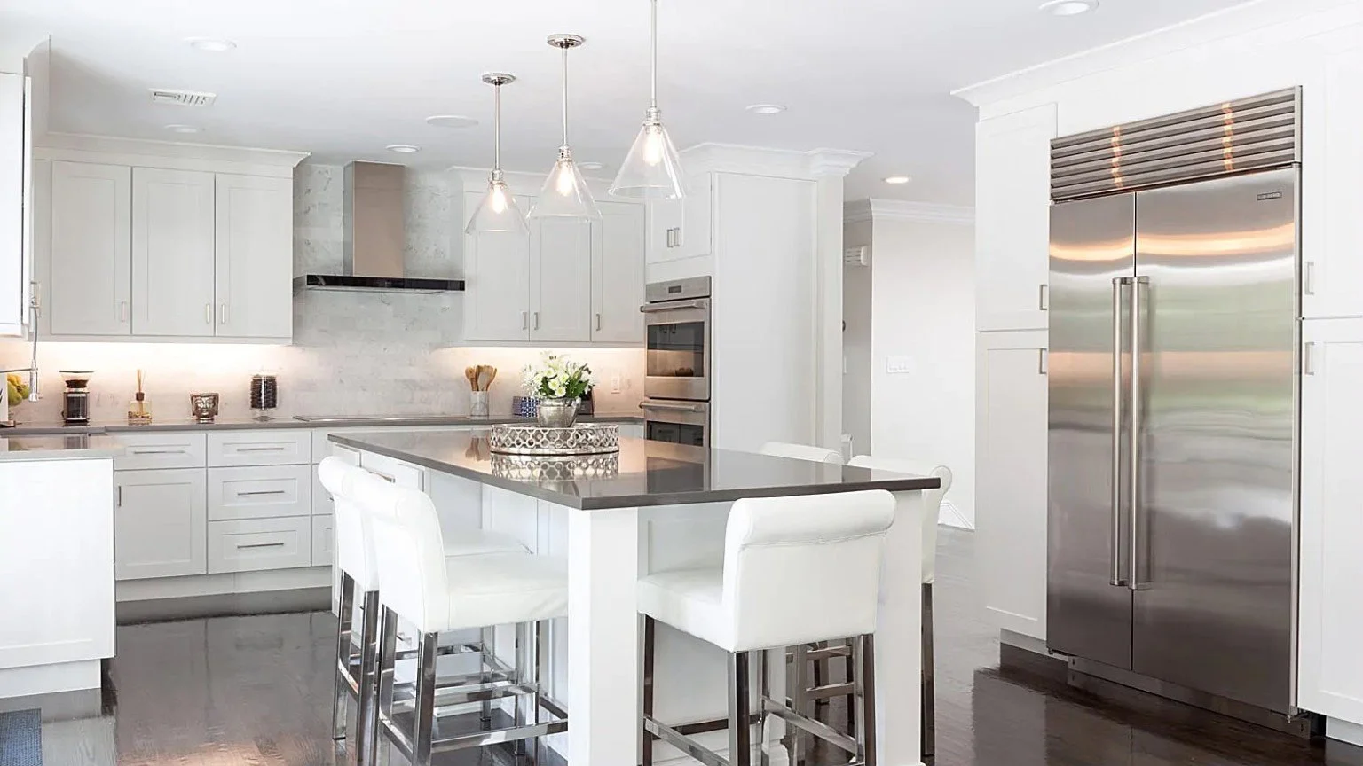 White kitchen with an island, pendant lighting, and stainless steel appliances.