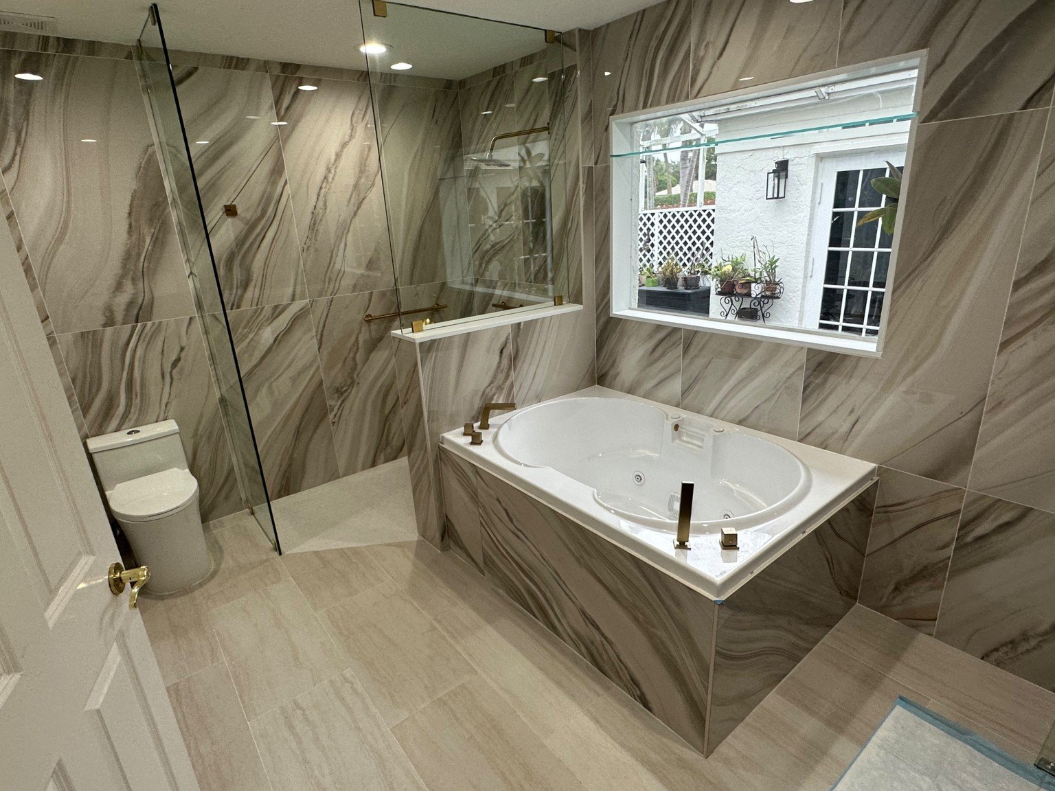 Bathroom renovation with a soaking tub, glass shower, and warm gold fixtures.