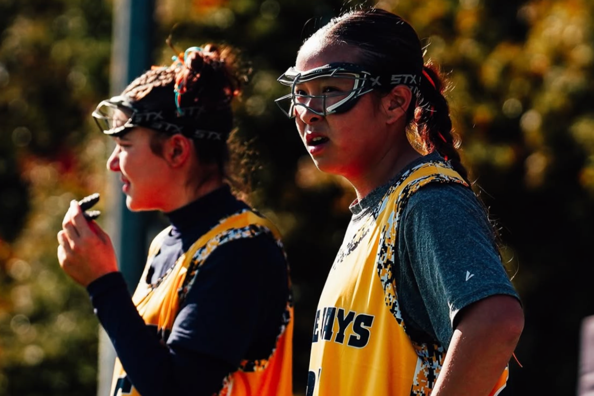 Two young female athletes wearing yellow and black sports jerseys and protective goggles during an outdoor sports event.