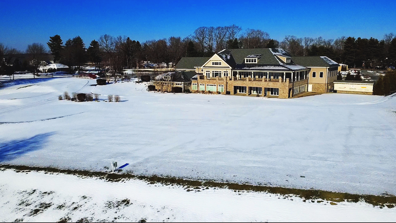 A large house with multiple levels and a green roof surrounded by snowy landscape and trees under a clear blue sky.
