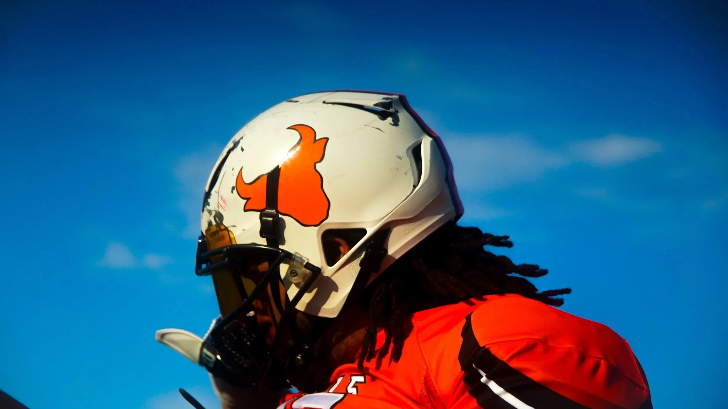 A person wearing a white helmet with an orange logo and an orange shirt, with the sky in the background.