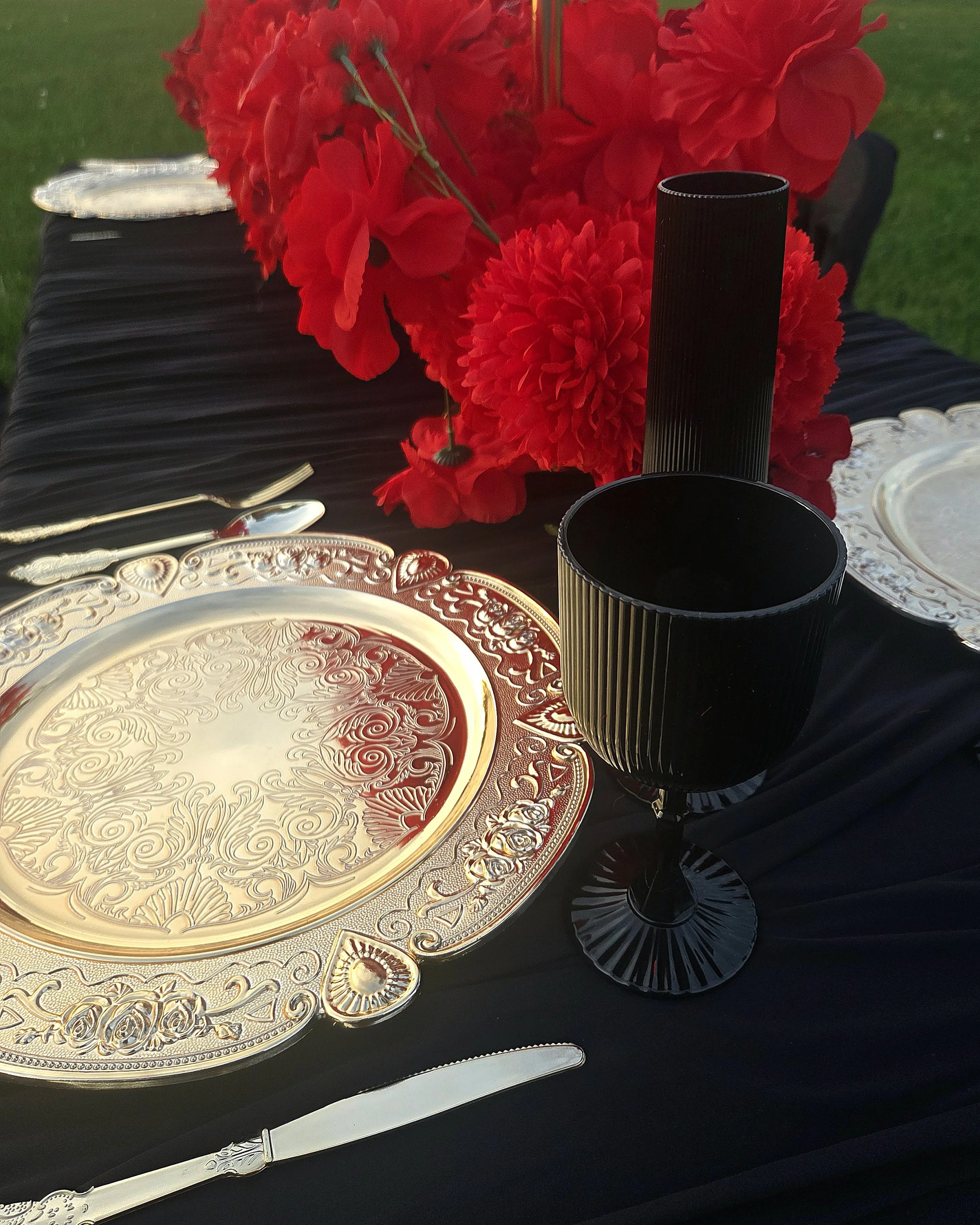 A table setting with a decorative gold and silver tray, a black vase, and a bouquet of red flowers, including roses and carnations, on a black tablecloth.