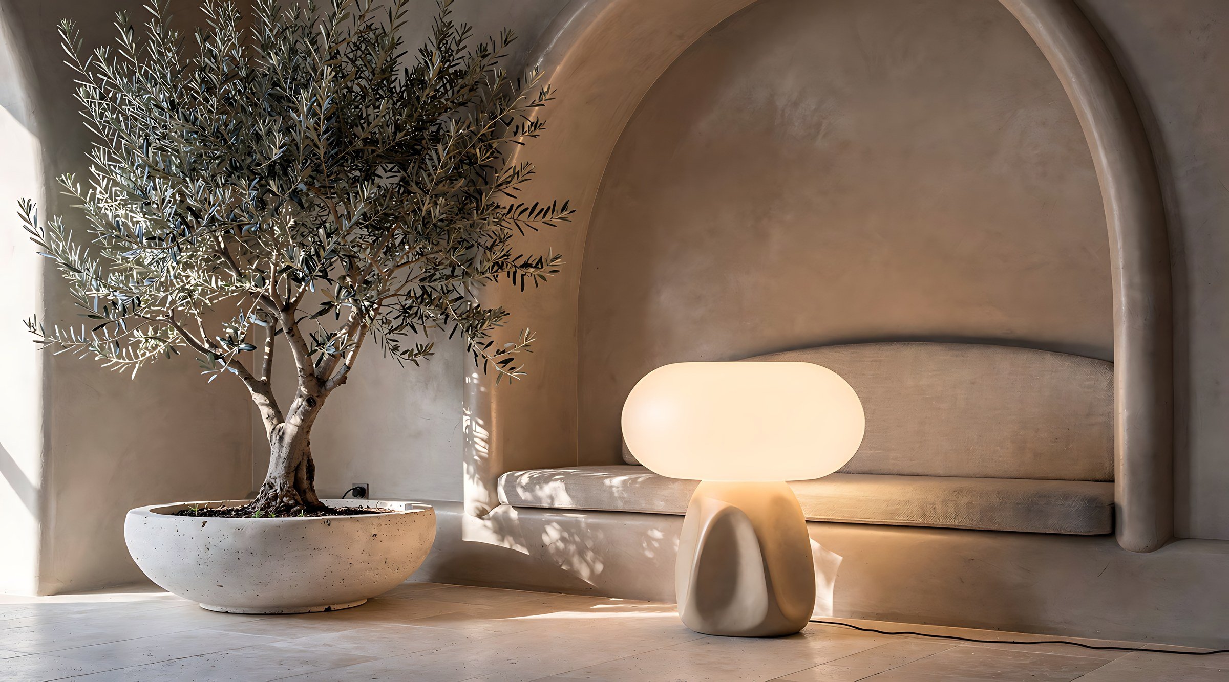 Olive tree in a stone planter beside a softly glowing lamp in a calm arched nook